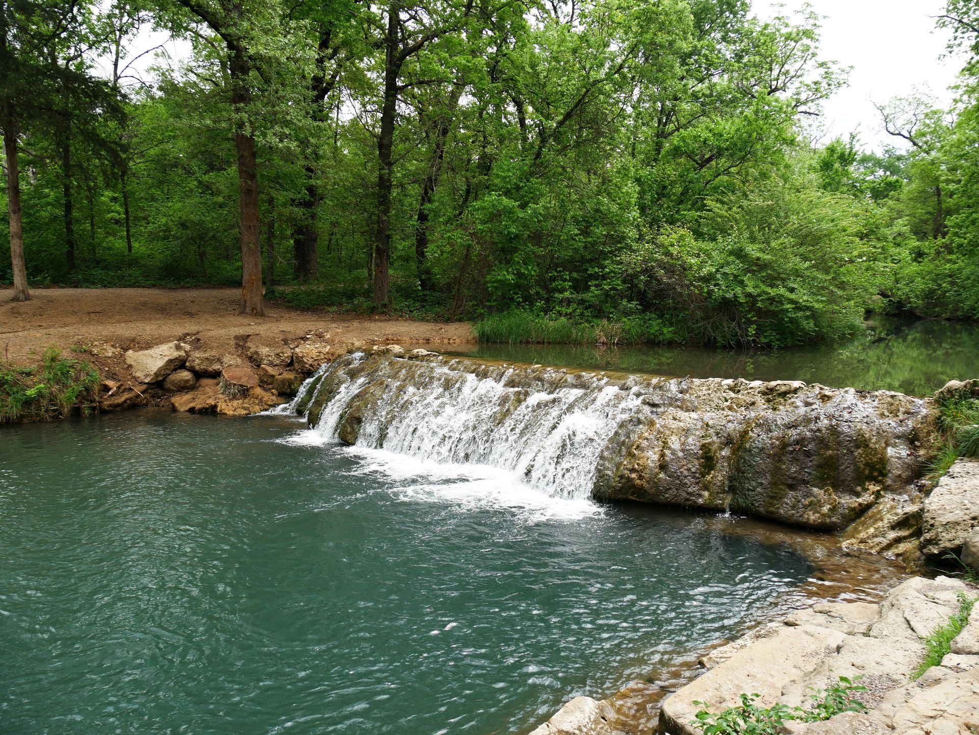 A small waterfall is surrounded by trees and rocks in a river.