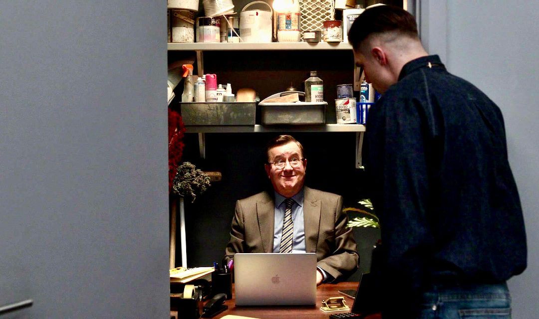 A man in a suit is sitting at a desk with a laptop.