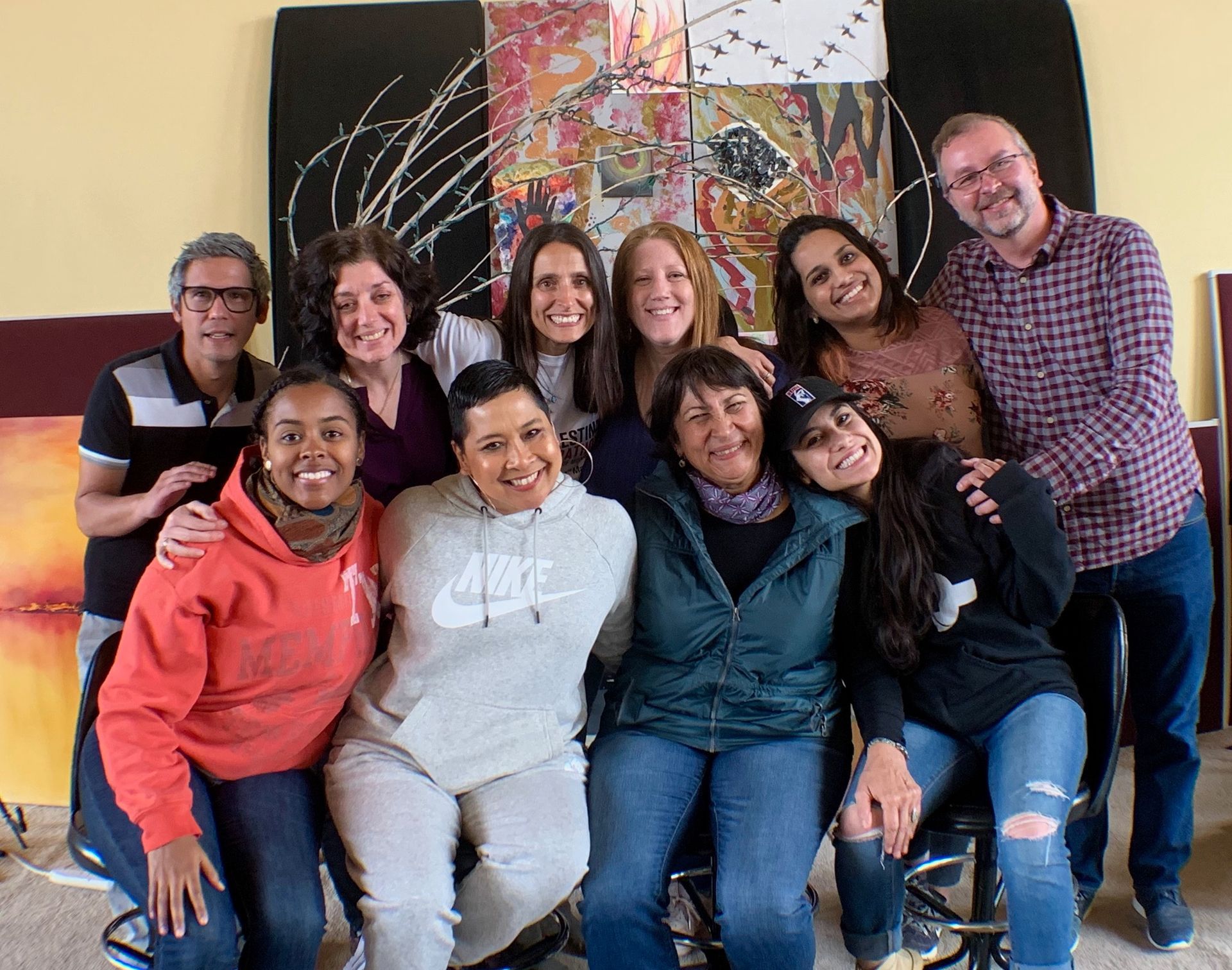 A group of people are posing for a picture in front of a painting.