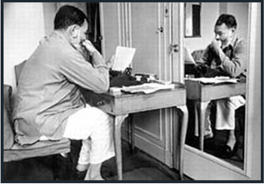 A black and white photo of a man sitting at a desk using a typewriter