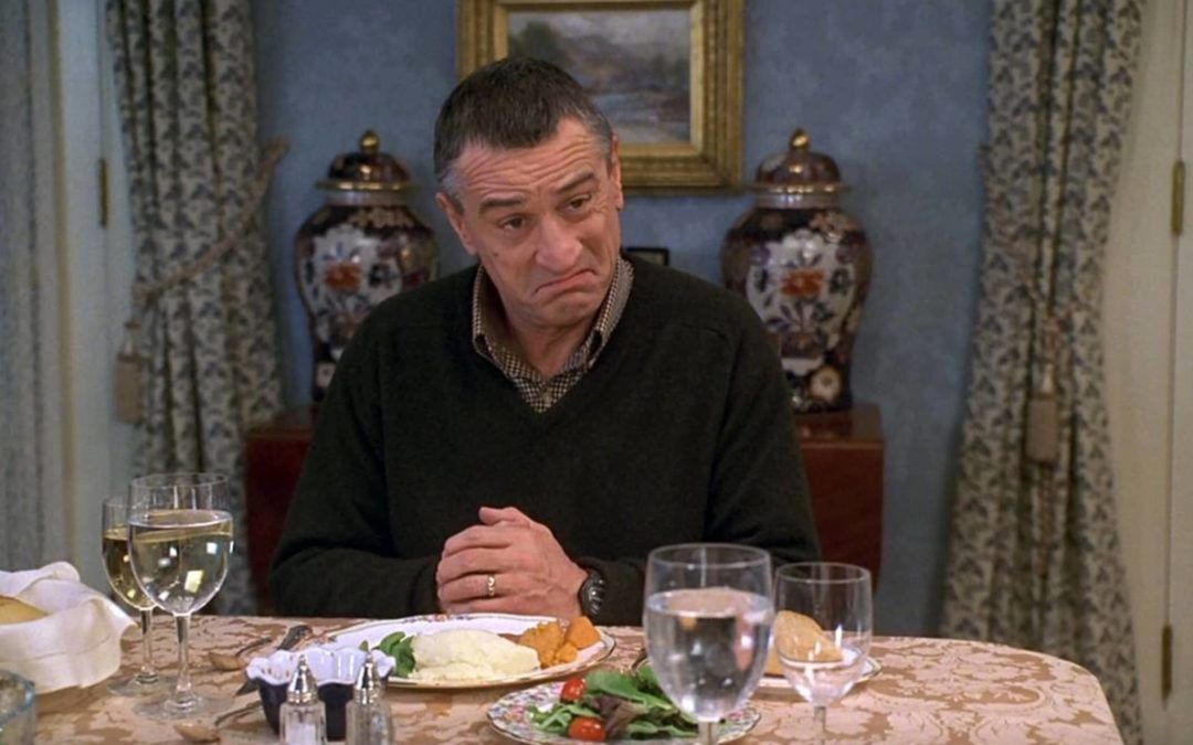 A man is sitting at a table with plates of food and wine glasses.