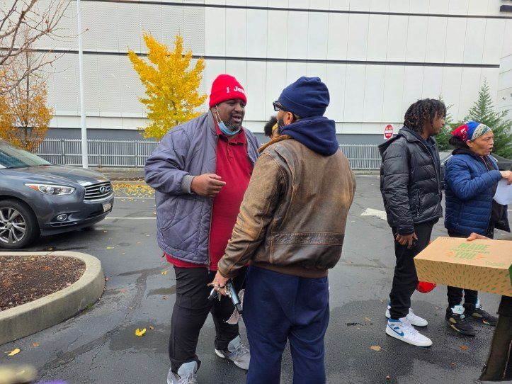 People talking outdoors; one in red hat. Autumn trees, cars and a building in the background.