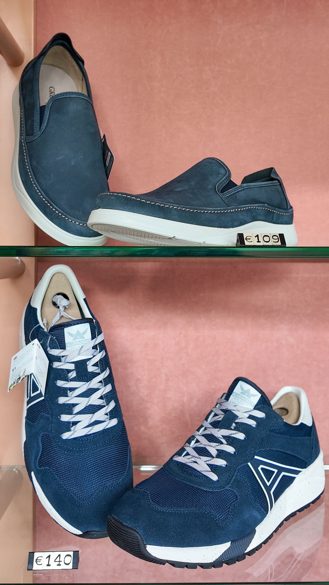 Scarpe esposte sugli scaffali: due paia di slip-on blu e due scarpe da ginnastica blu con suola bianca.