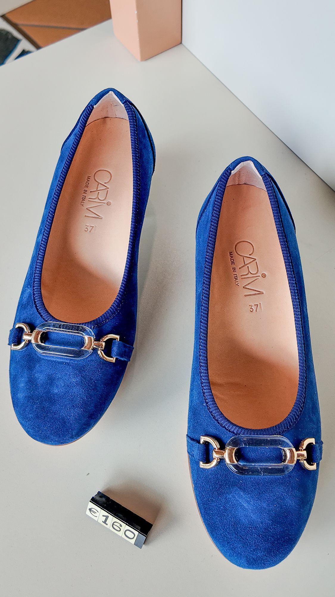 Ballerine in pelle scamosciata blu con fibbie dorate, appoggiate su una superficie chiara.