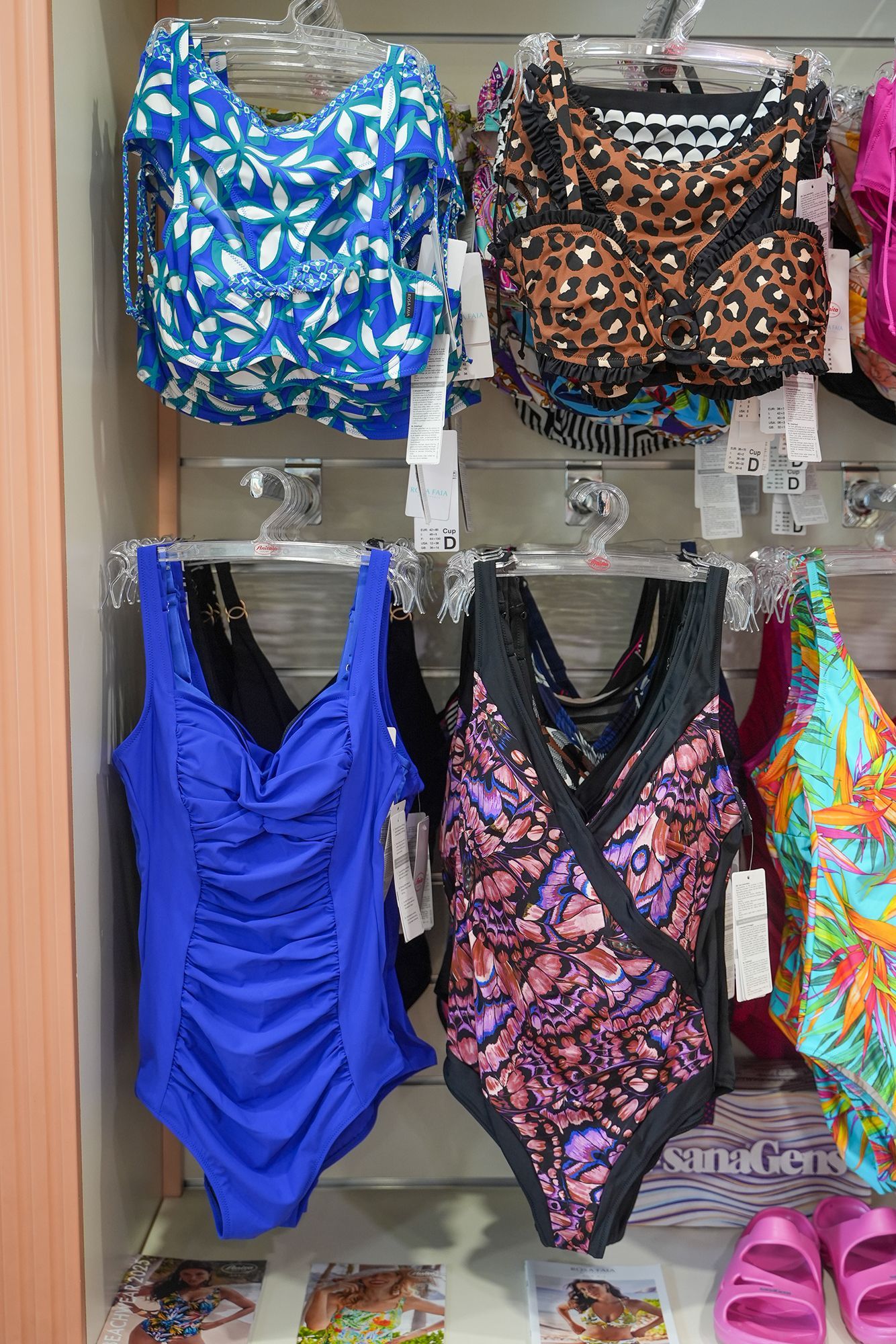 Costumi da bagno esposti in un negozio, tra cui modelli interi blu a fiori, leopardati e fantasia.