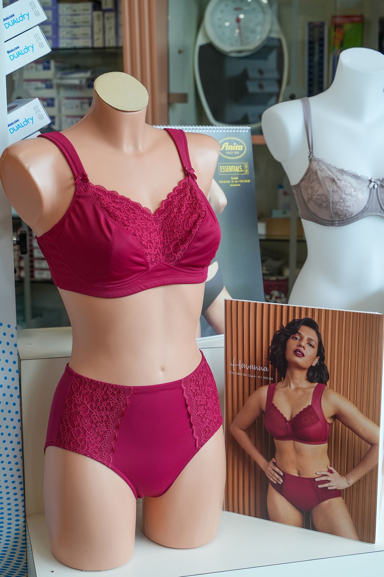 Manichino con reggiseno bordeaux e slip a vita alta. Accanto a un poster e un reggiseno su un altro manichino.