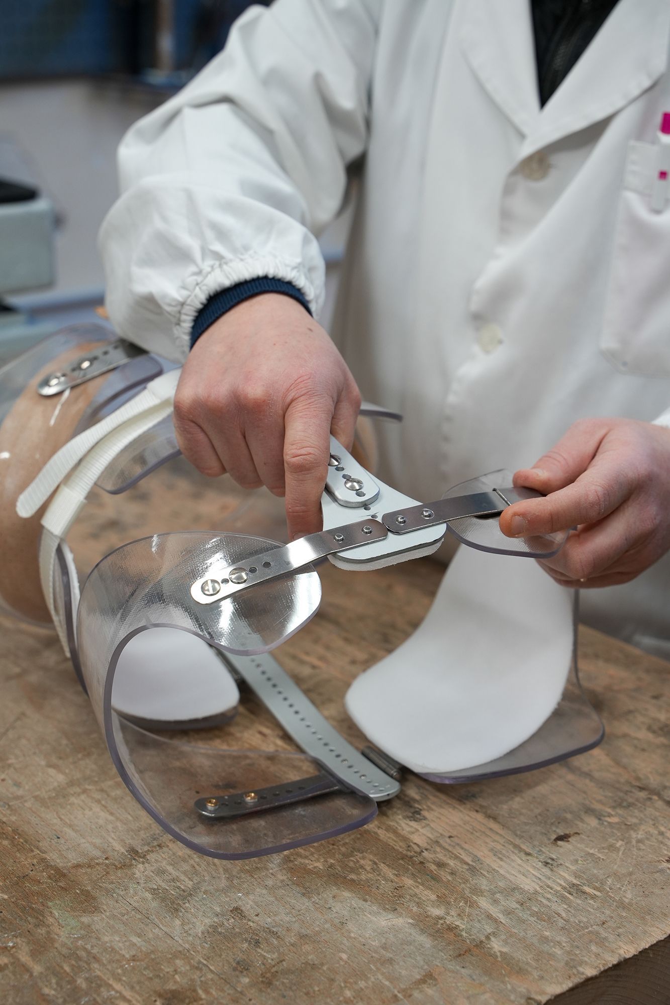 Una persona in camice regola un tutore ortopedico trasparente, utilizzando un righello di metallo su una superficie di legno.