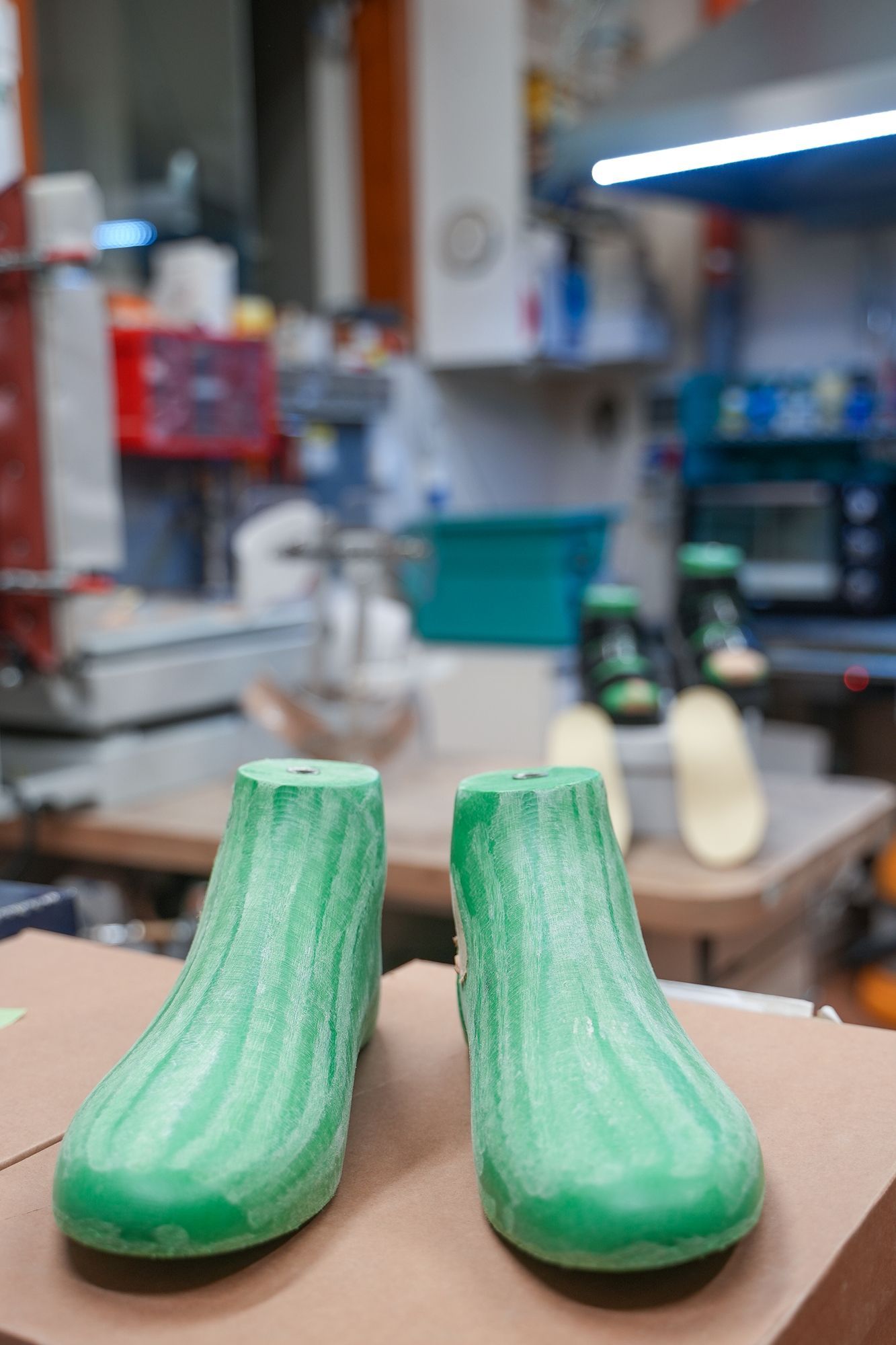 Forme di scarpe verdi su una superficie di cartone, con uno sfondo sfocato da officina.