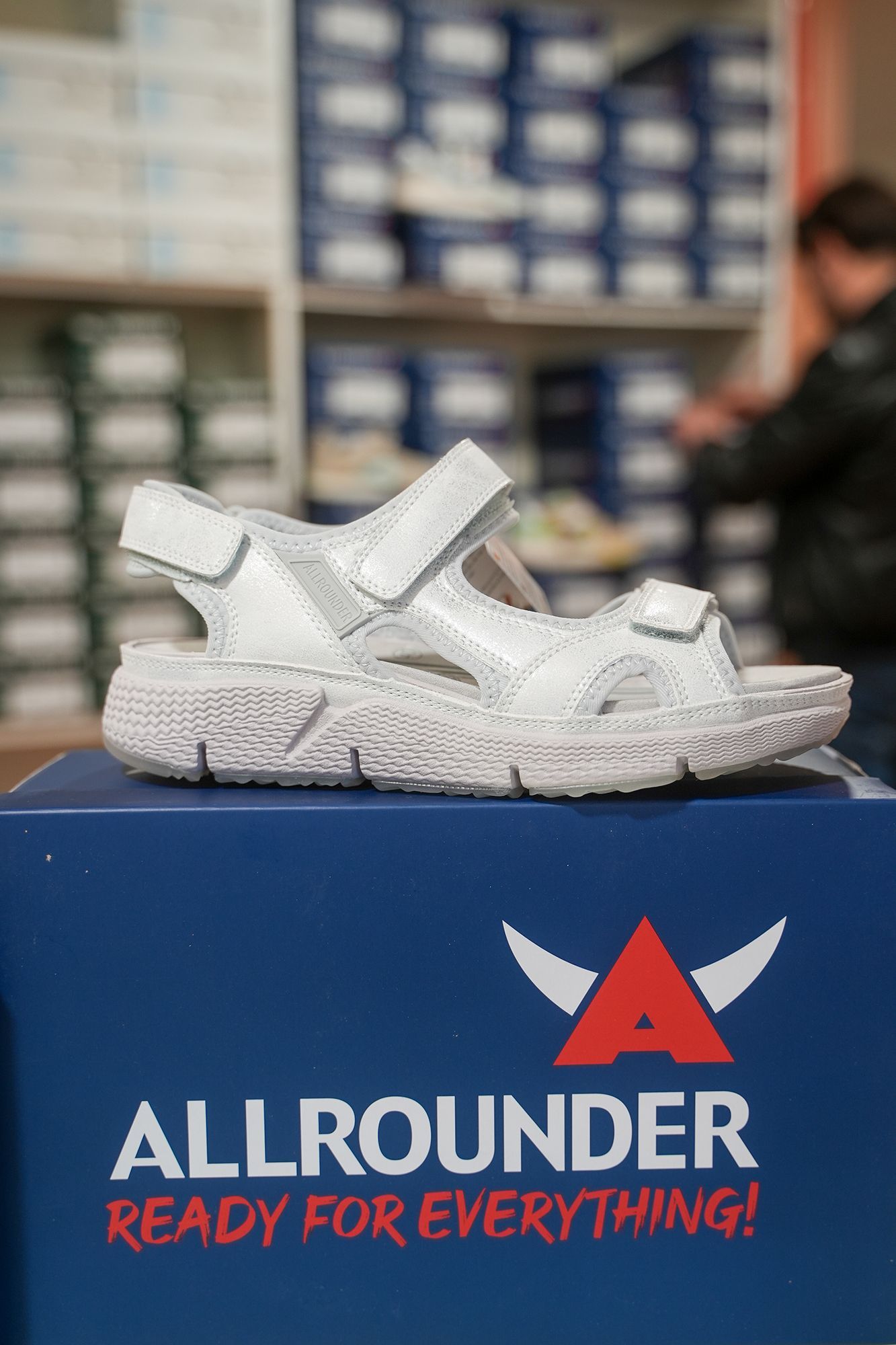 Sandalo bianco su una scatola Allrounder blu con lo slogan 