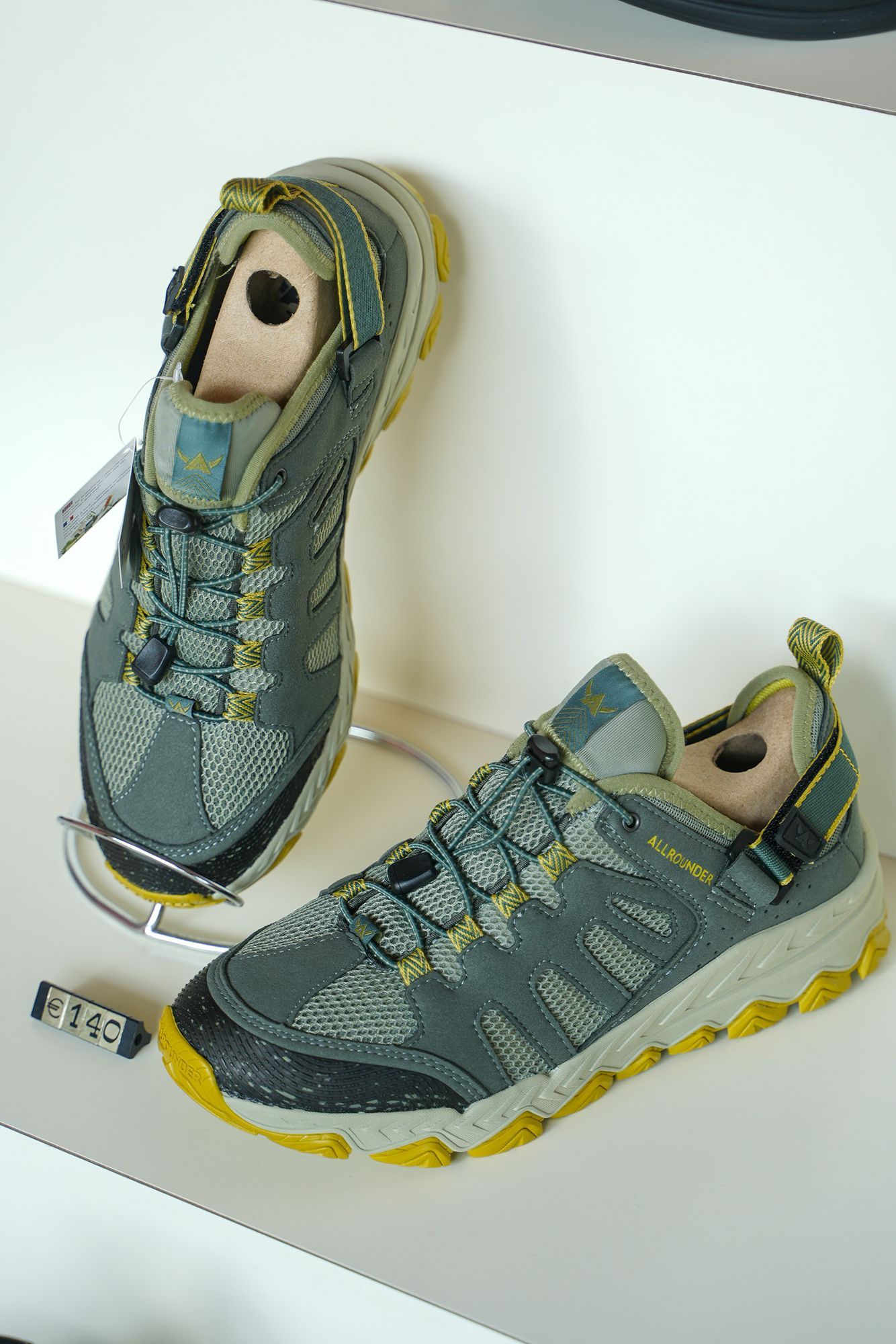 Un paio di scarpe da esterno grigie e gialle con tendiscarpe esposte su uno scaffale.