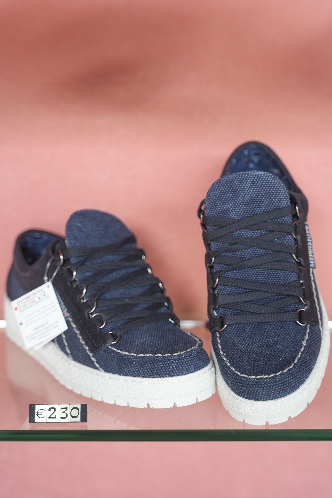 Sneakers in denim blu con suola bianca, esposte su uno scaffale con un'etichetta con il prezzo.