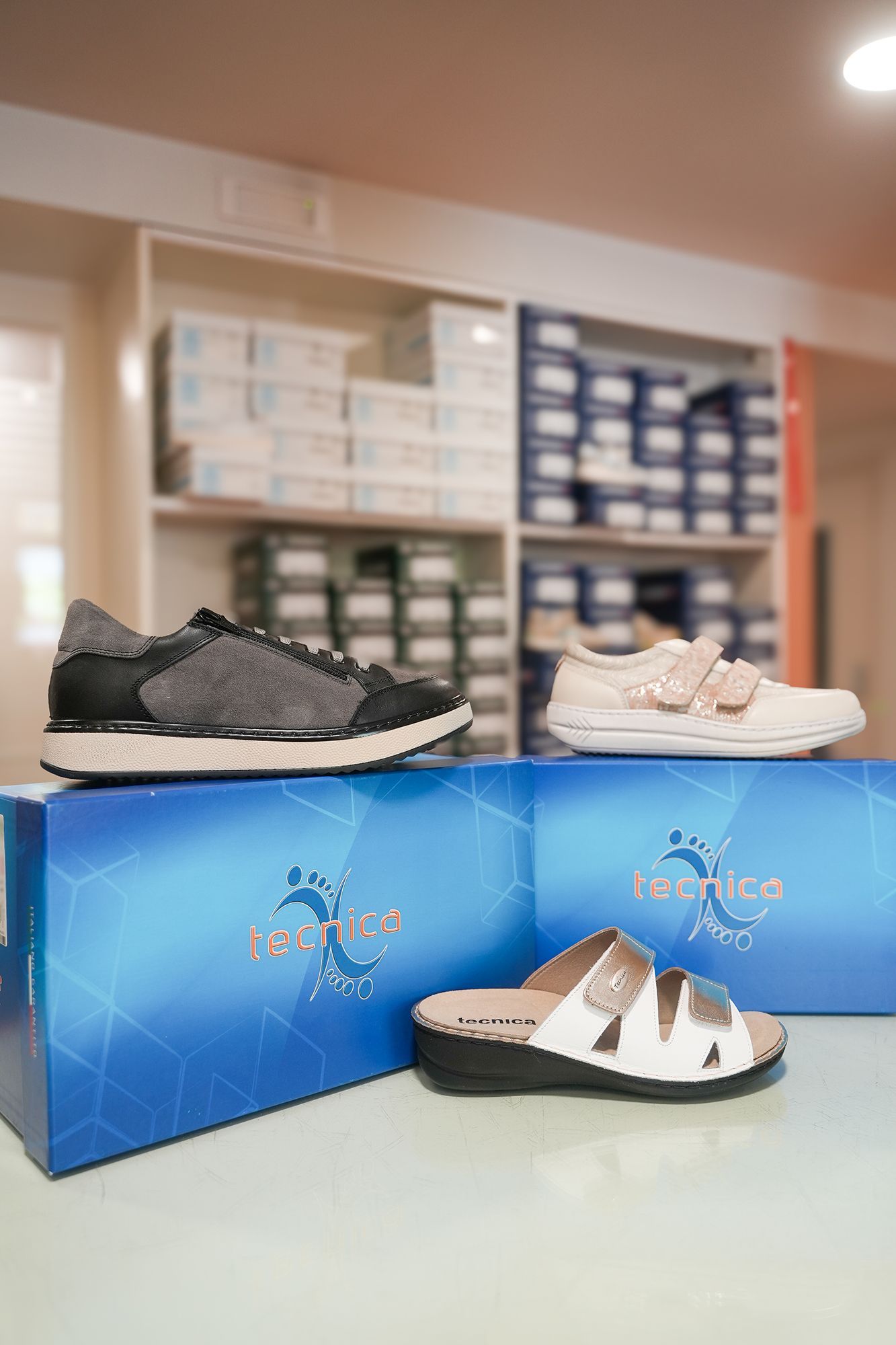 Scarpe su scatole blu in un negozio: sneaker bianche e nere, scarpa bianca con velcro, ciabatte bianche. Scaffali sullo sfondo.