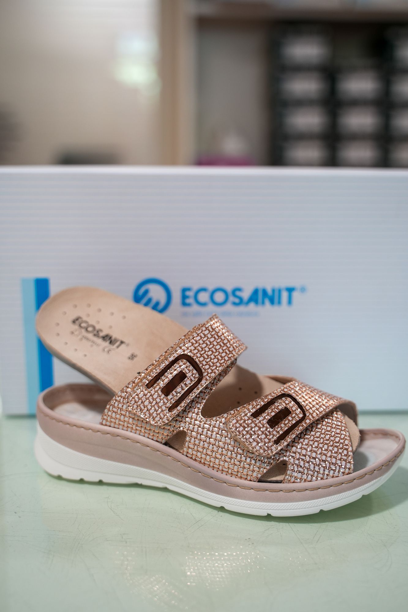Davanti alla scatola delle scarpe con il marchio sono presenti dei sandali Ecosanit color oro rosa con cinturini regolabili.
