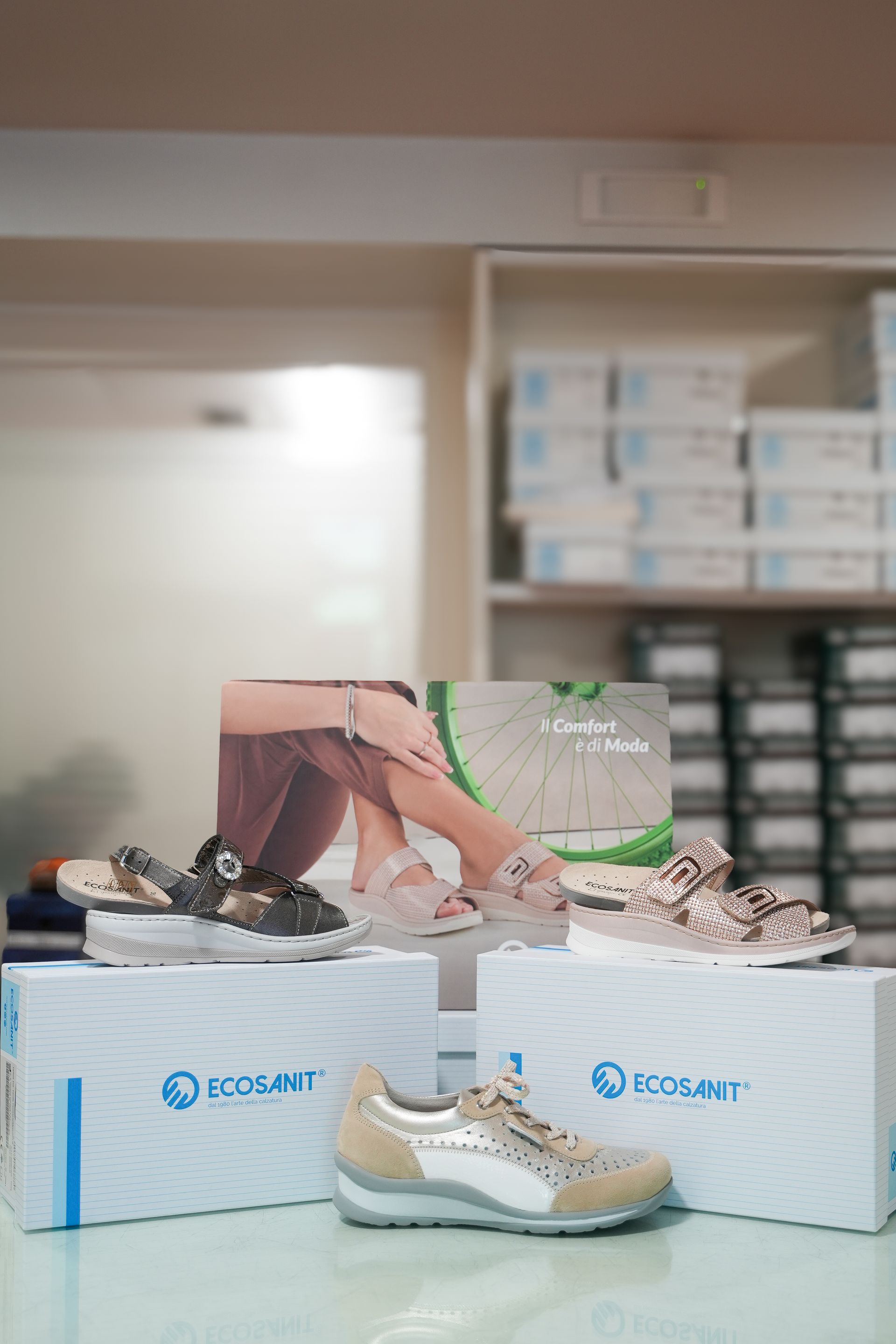 Scarpe esposte su una piattaforma bianca, con un poster di gambe che indossano sandali, in un ambiente da negozio.