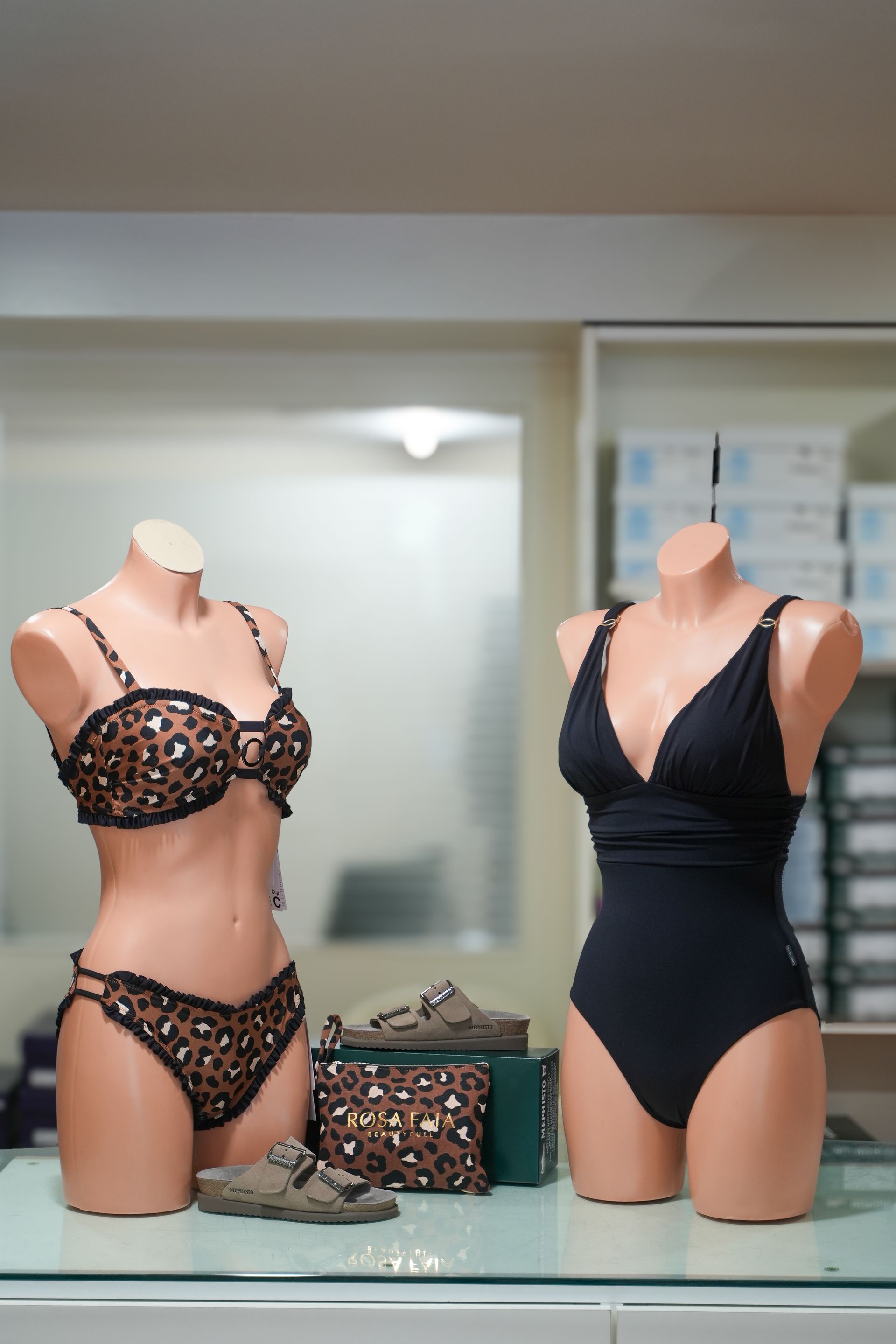 Due manichini espongono costumi da bagno: bikini leopardato e costume intero nero. Scarpe e borsa sono in mostra.