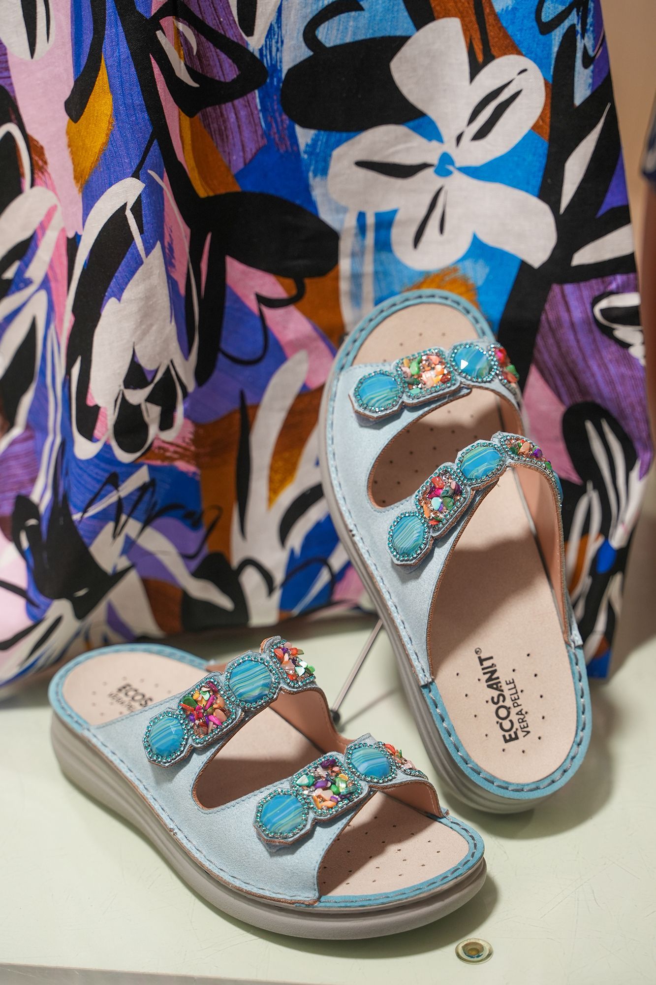 Sandali azzurri con dettagli di gemme color turchese su una stampa floreale colorata.