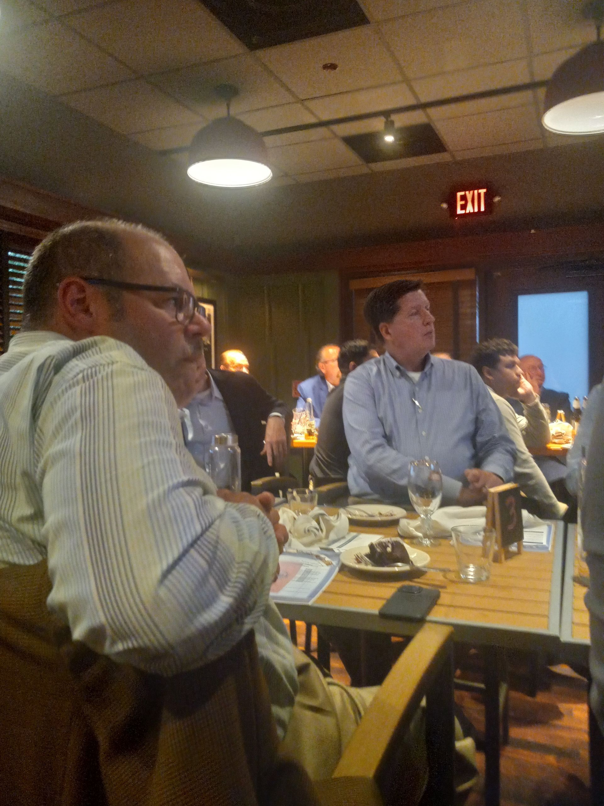 A group of men are sitting at a table in front of an exit sign