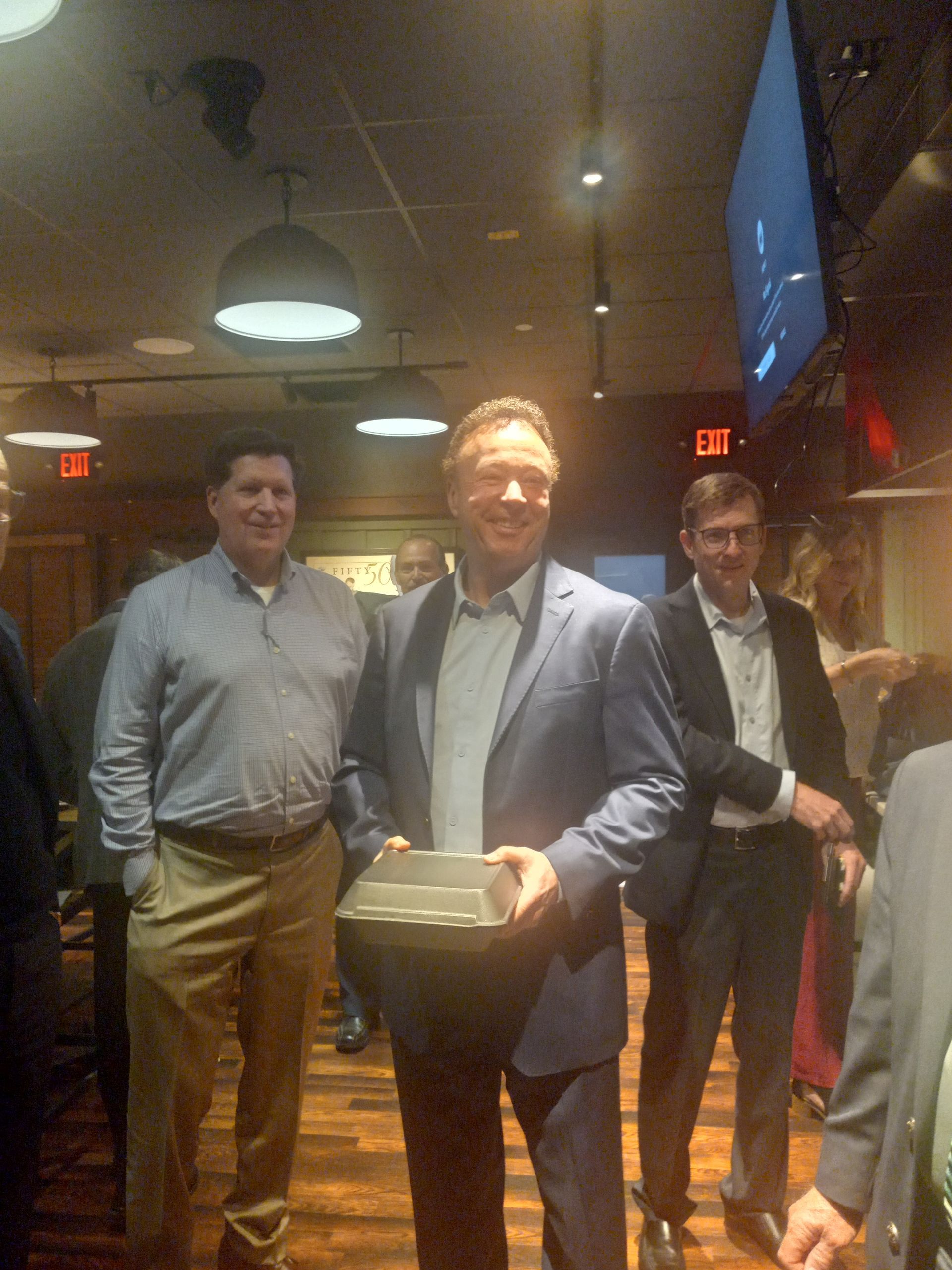 A group of men are standing in a room and one man is holding a box