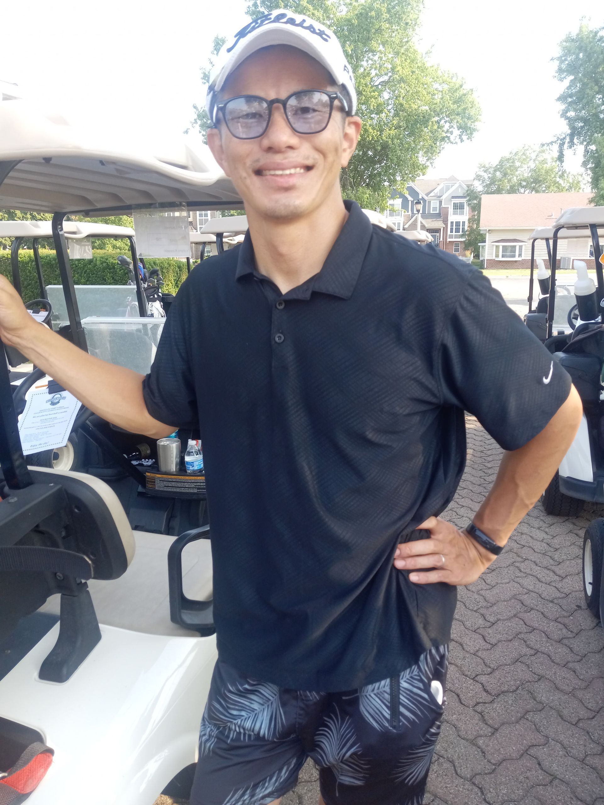 A man wearing glasses and a hat is standing next to a golf cart.