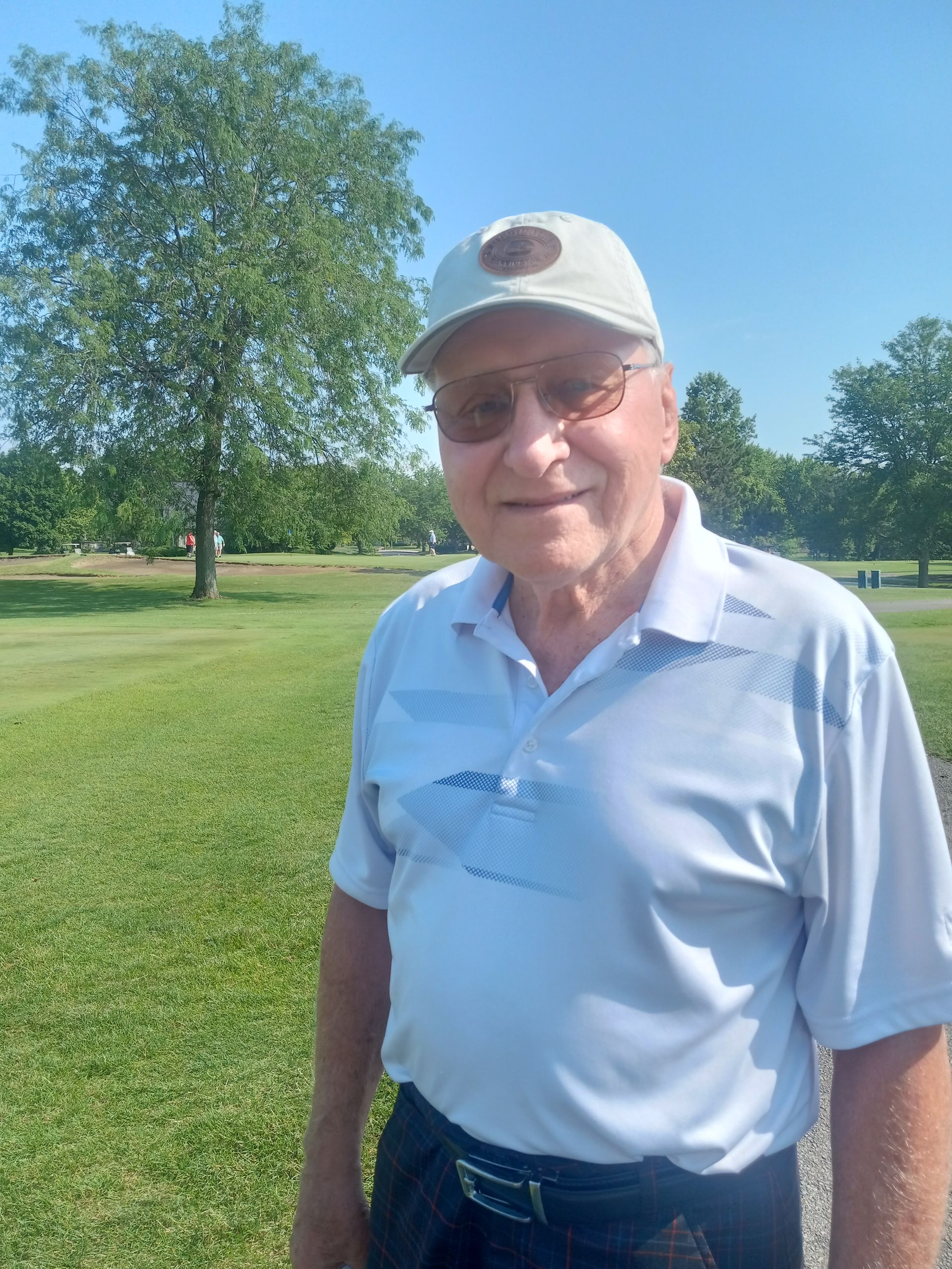 A man wearing a hat and sunglasses is standing in a grassy field.