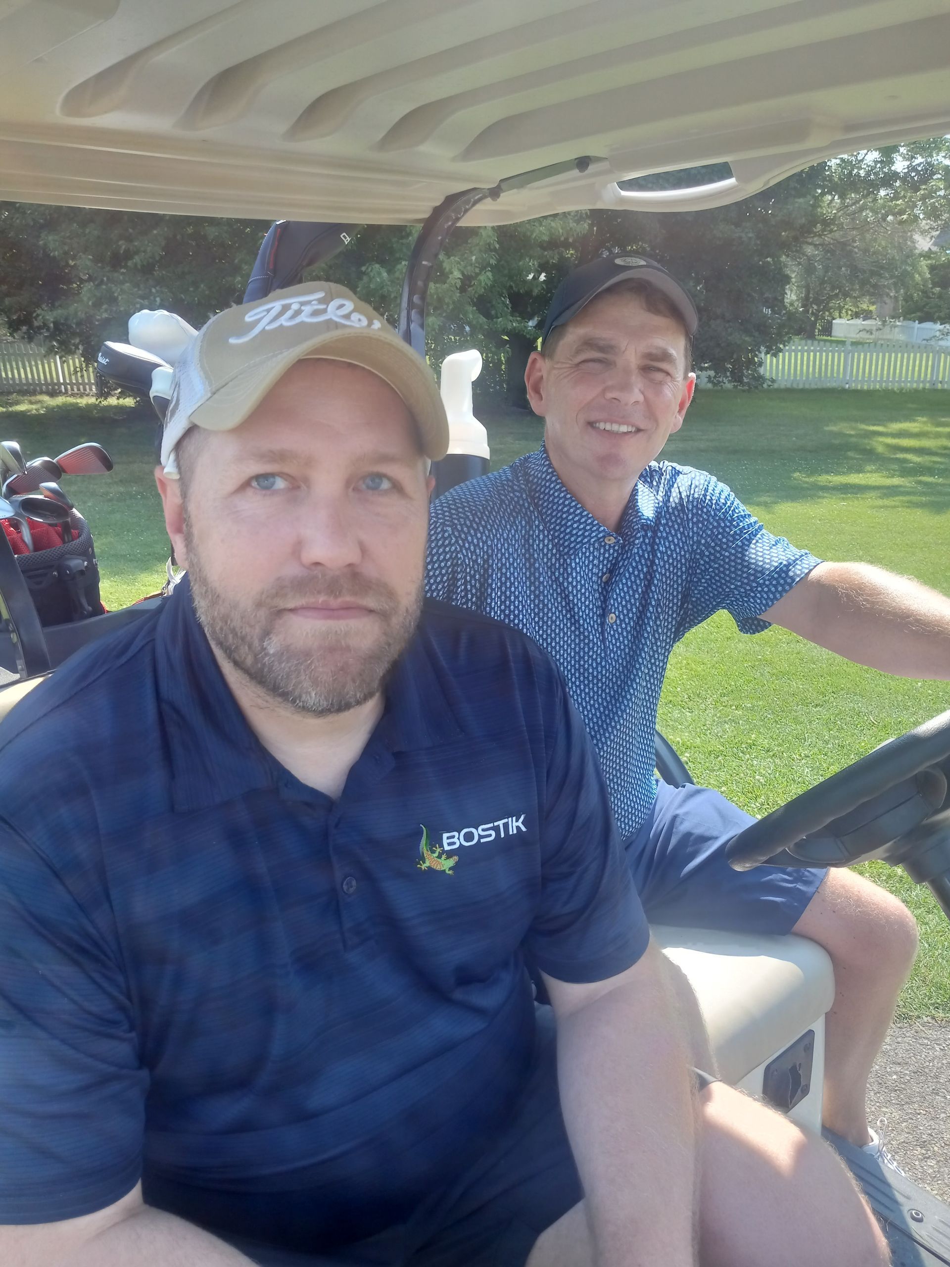 Two men are sitting in a golf cart and one of them is wearing a shirt that says lacoste