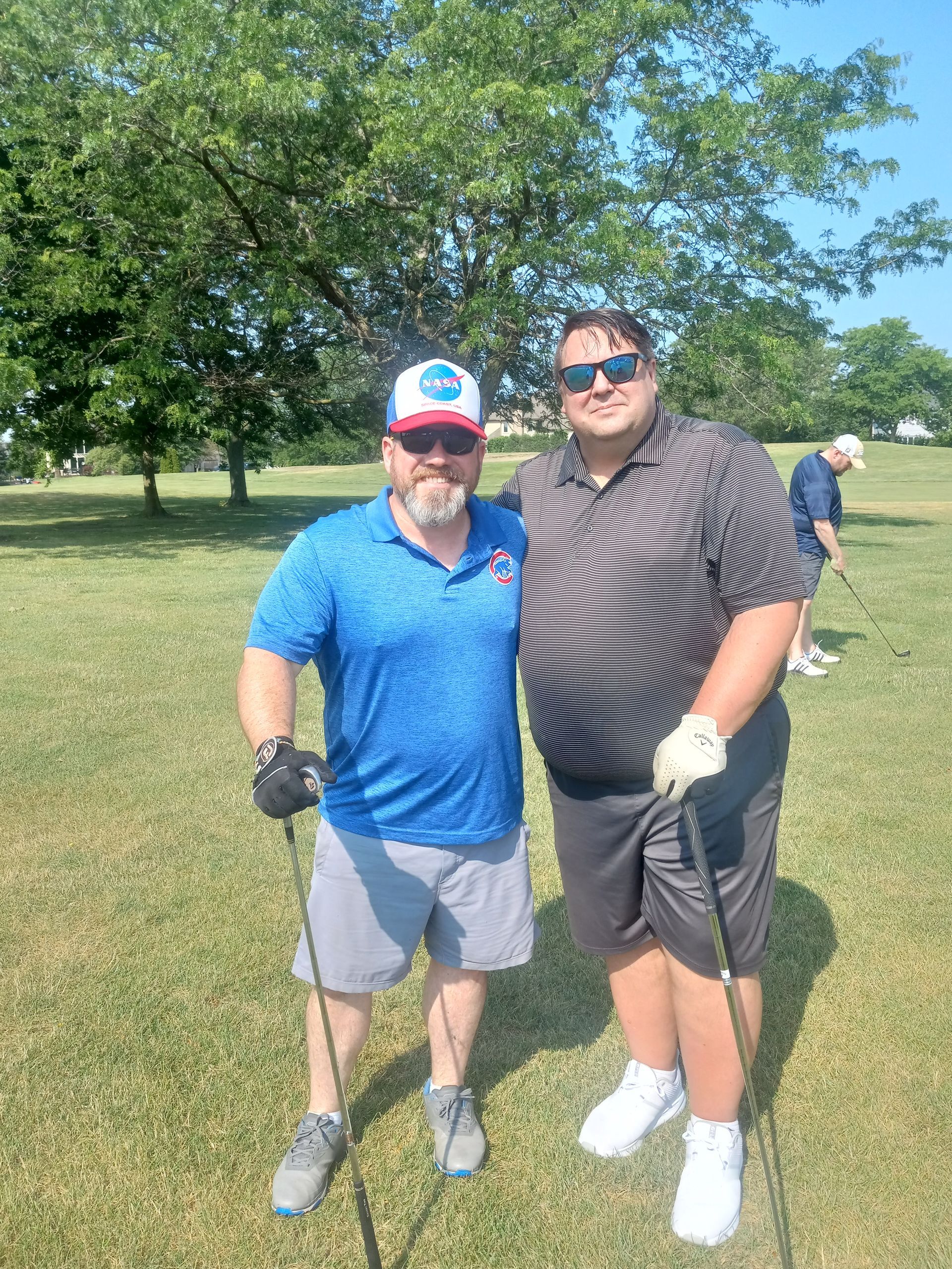 Two men are standing next to each other on a golf course holding golf clubs.