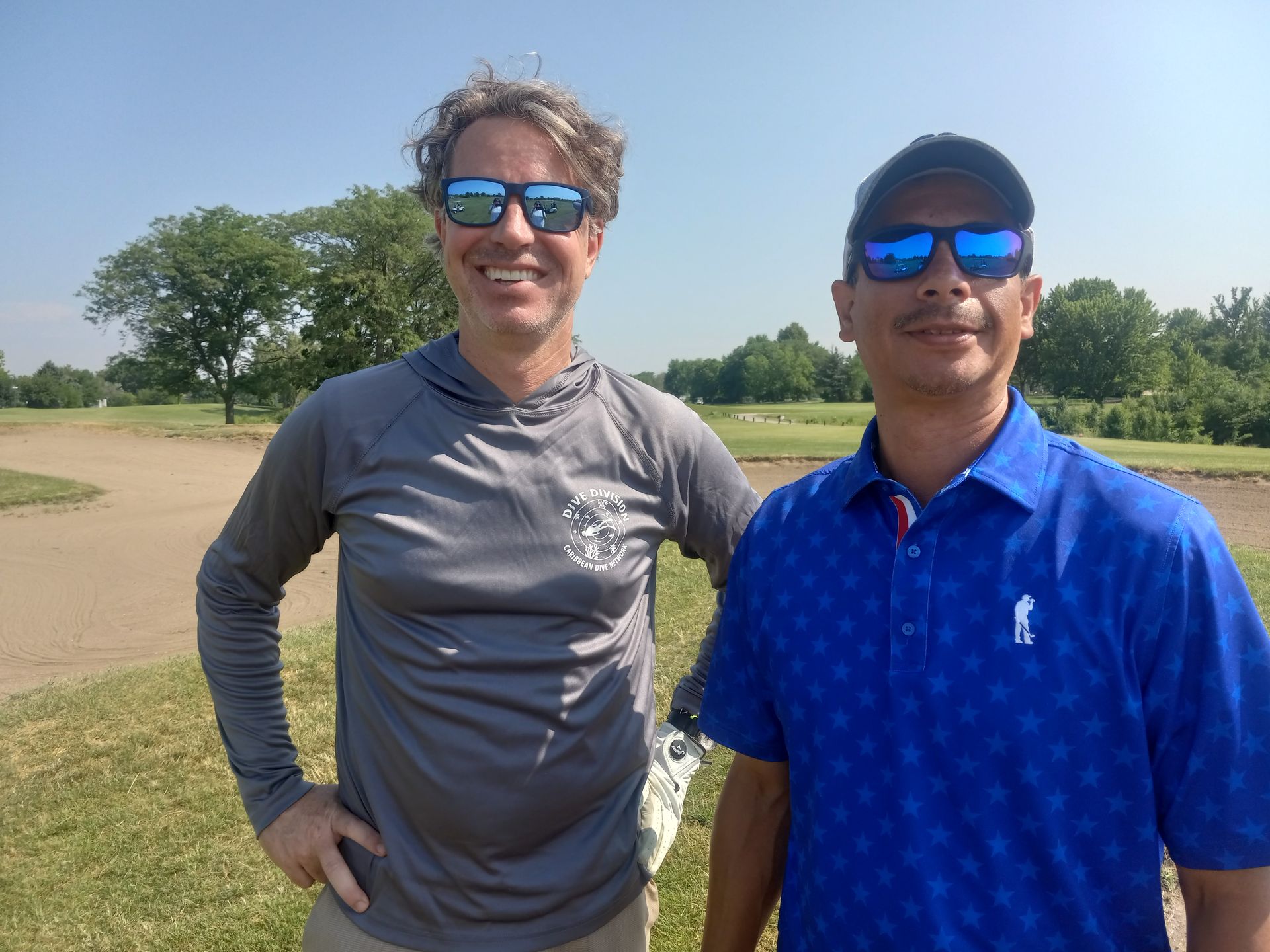 Two men wearing sunglasses are standing next to each other on a golf course