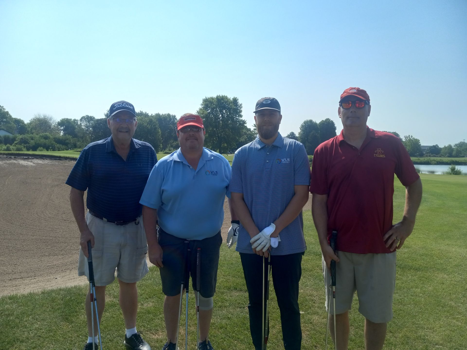 Four men are standing on a golf course holding golf clubs.