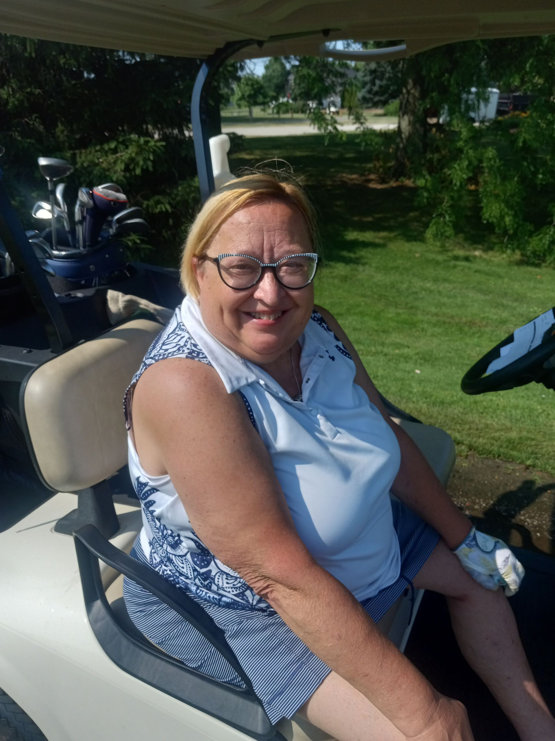 A woman wearing glasses is sitting in a golf cart.