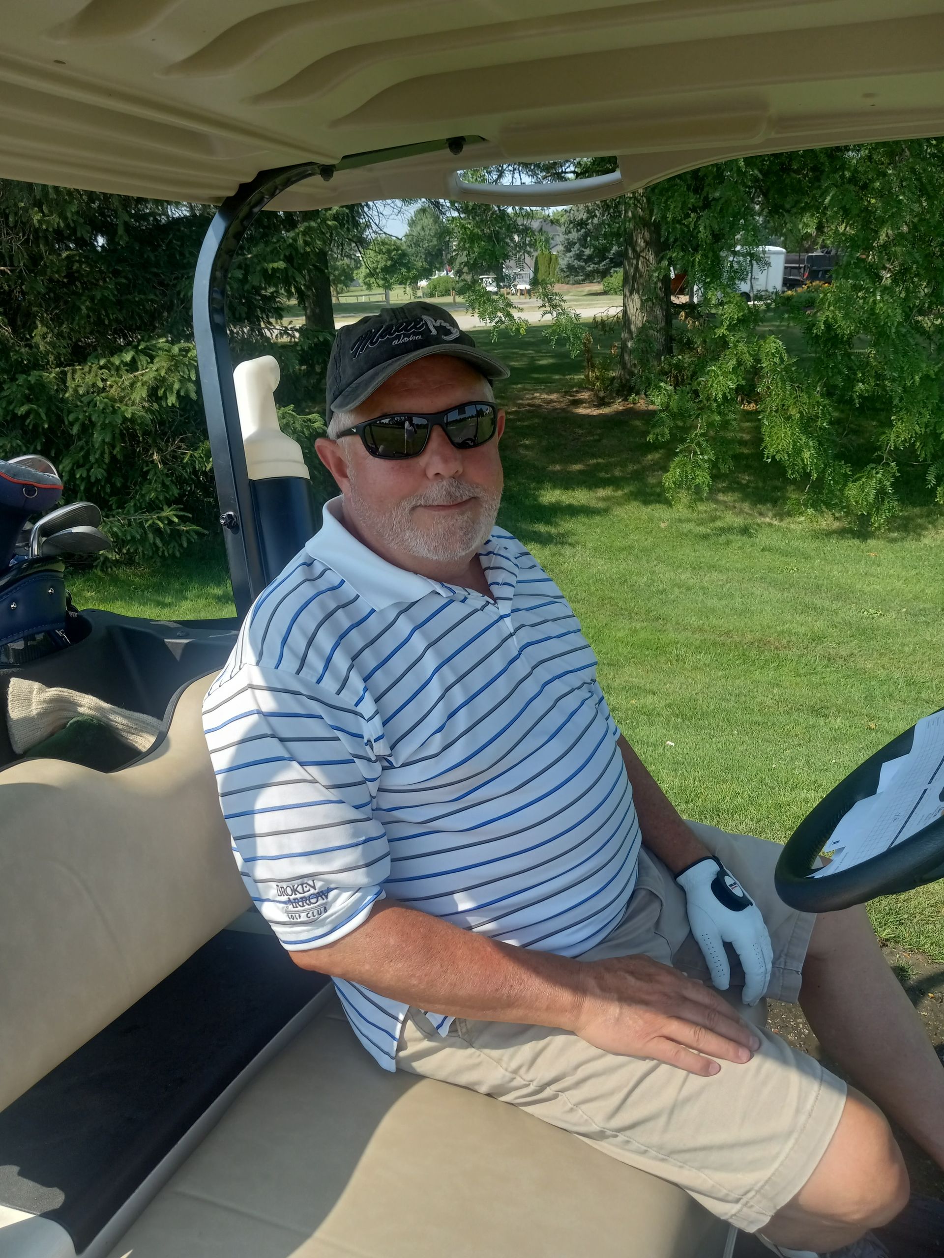 A man is sitting in a golf cart wearing sunglasses and a hat.