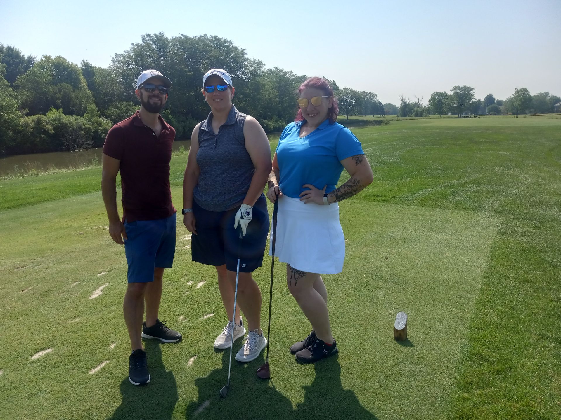 Three people are standing on a golf course holding golf clubs.