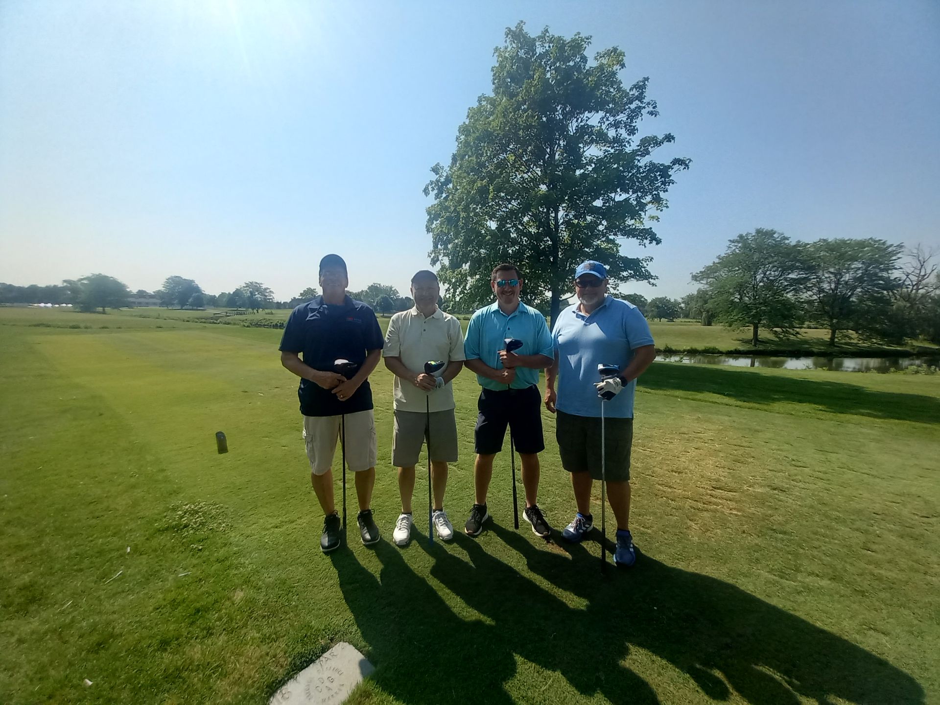 Four men are standing on a golf course holding golf clubs.