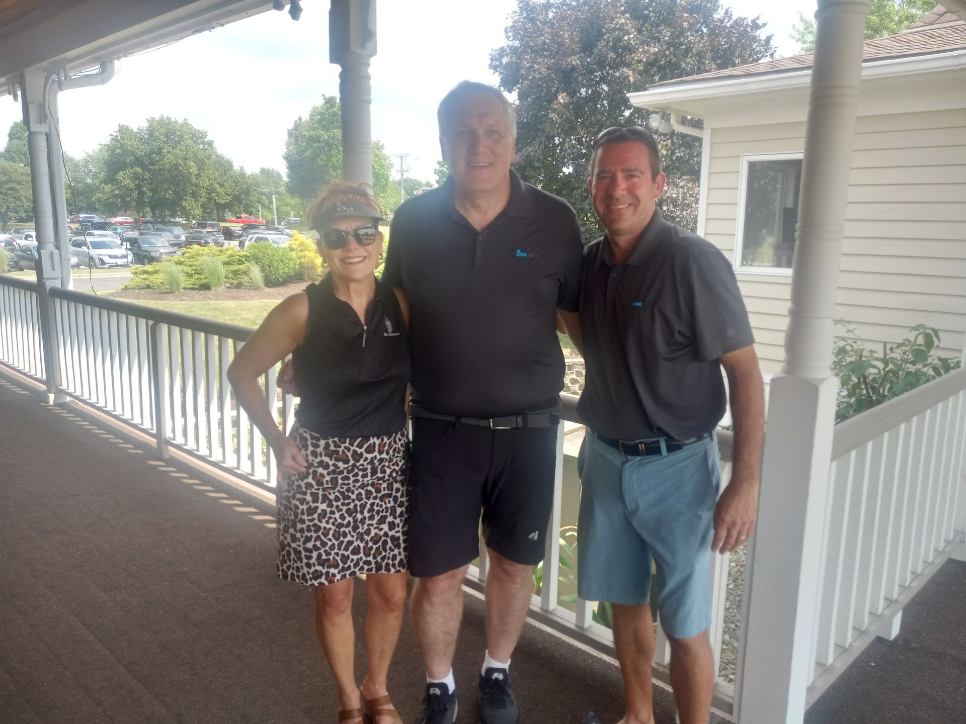 Two men and a woman are posing for a picture on a porch
