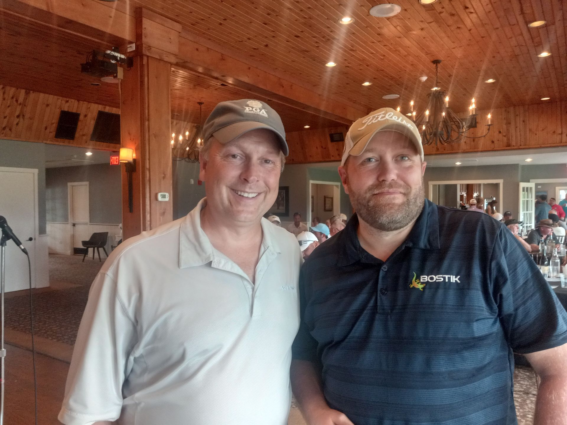 Two men are posing for a picture in a room with a wooden ceiling.