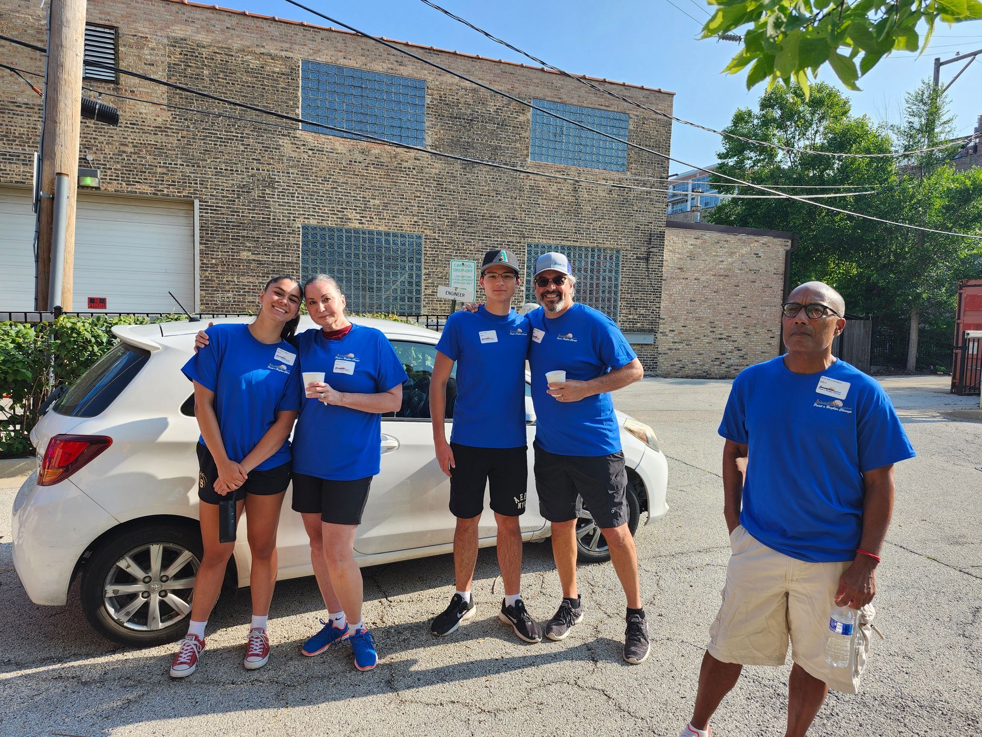 A group of people in blue shirts are posing for a picture in front of a white car.