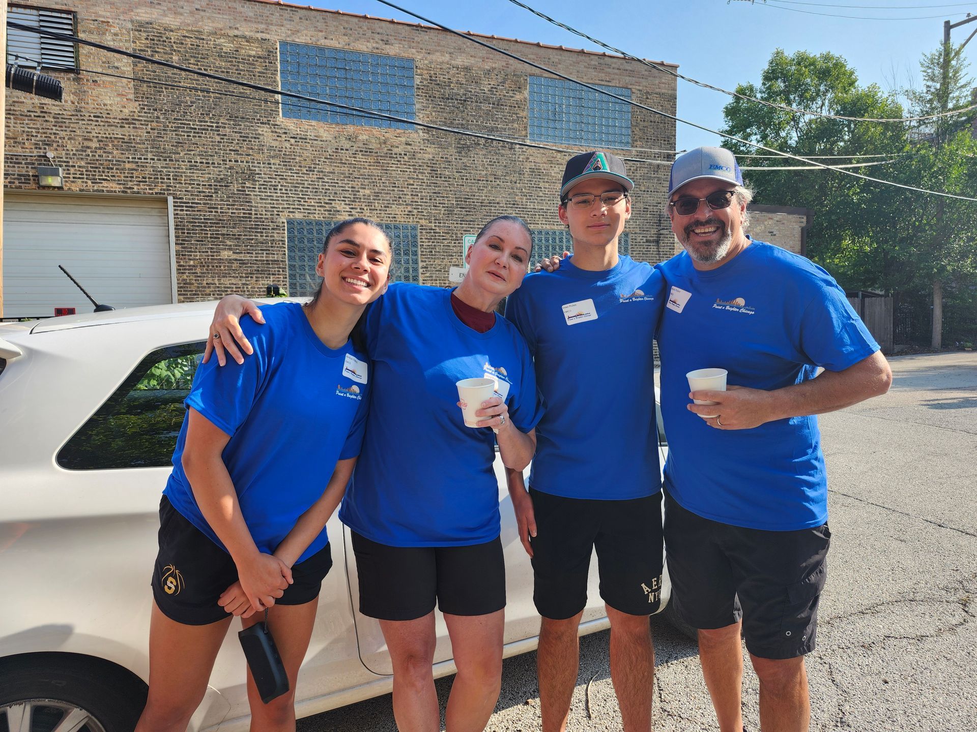 A group of people in blue shirts are posing for a picture in front of a white car.