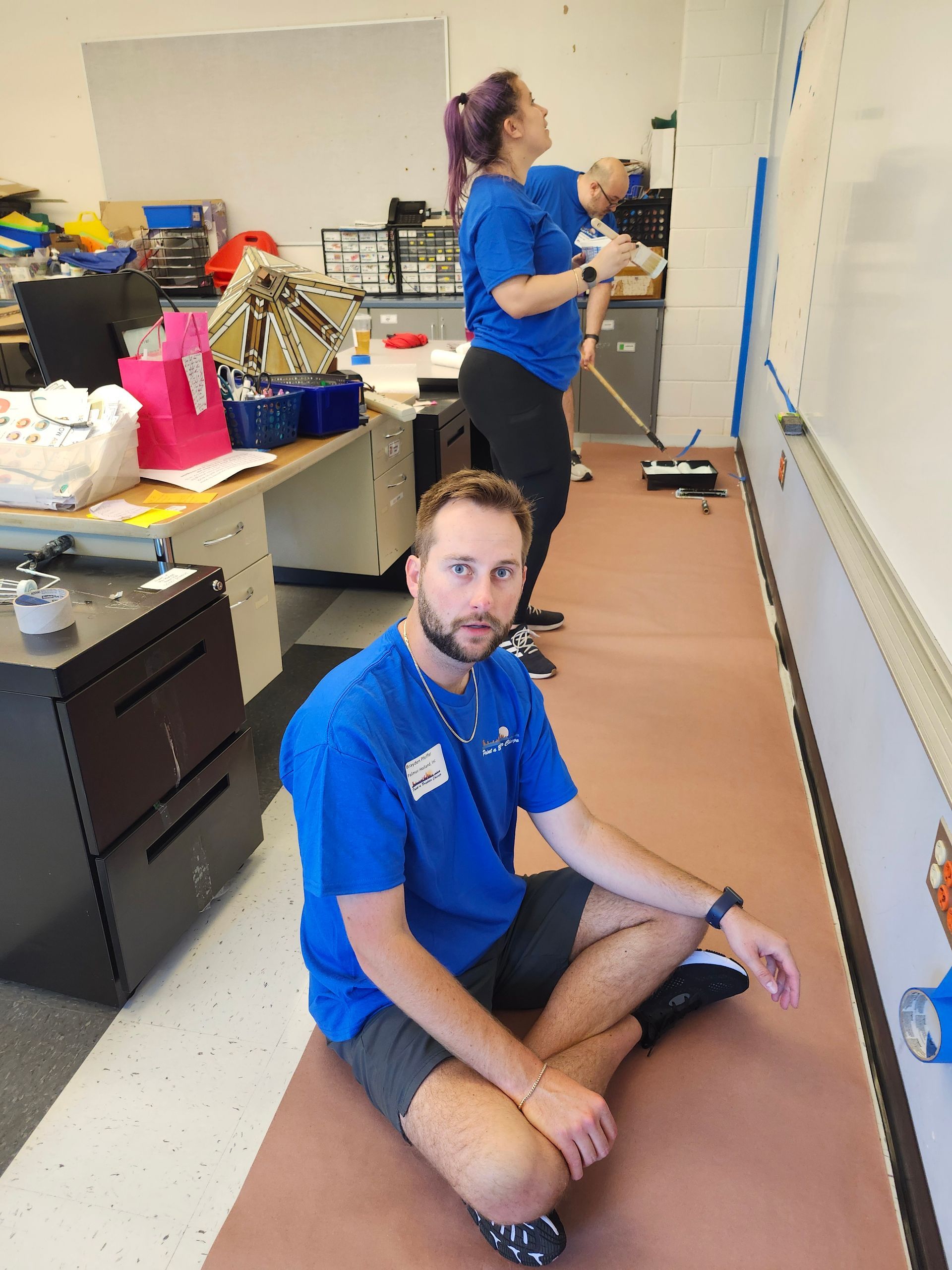 A man in a blue shirt is sitting on the floor in an office