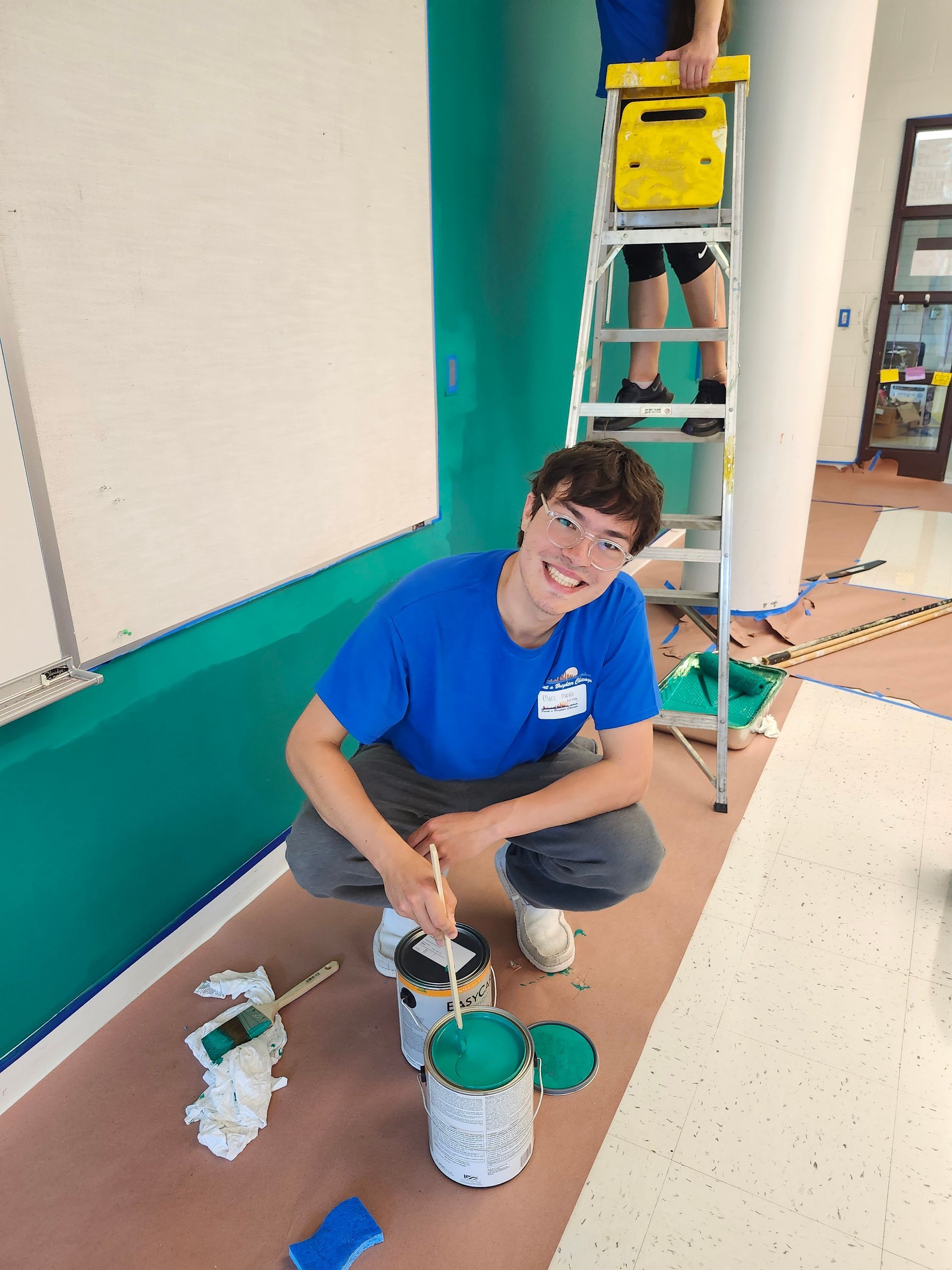 A man in a blue shirt is kneeling down and painting a wall.