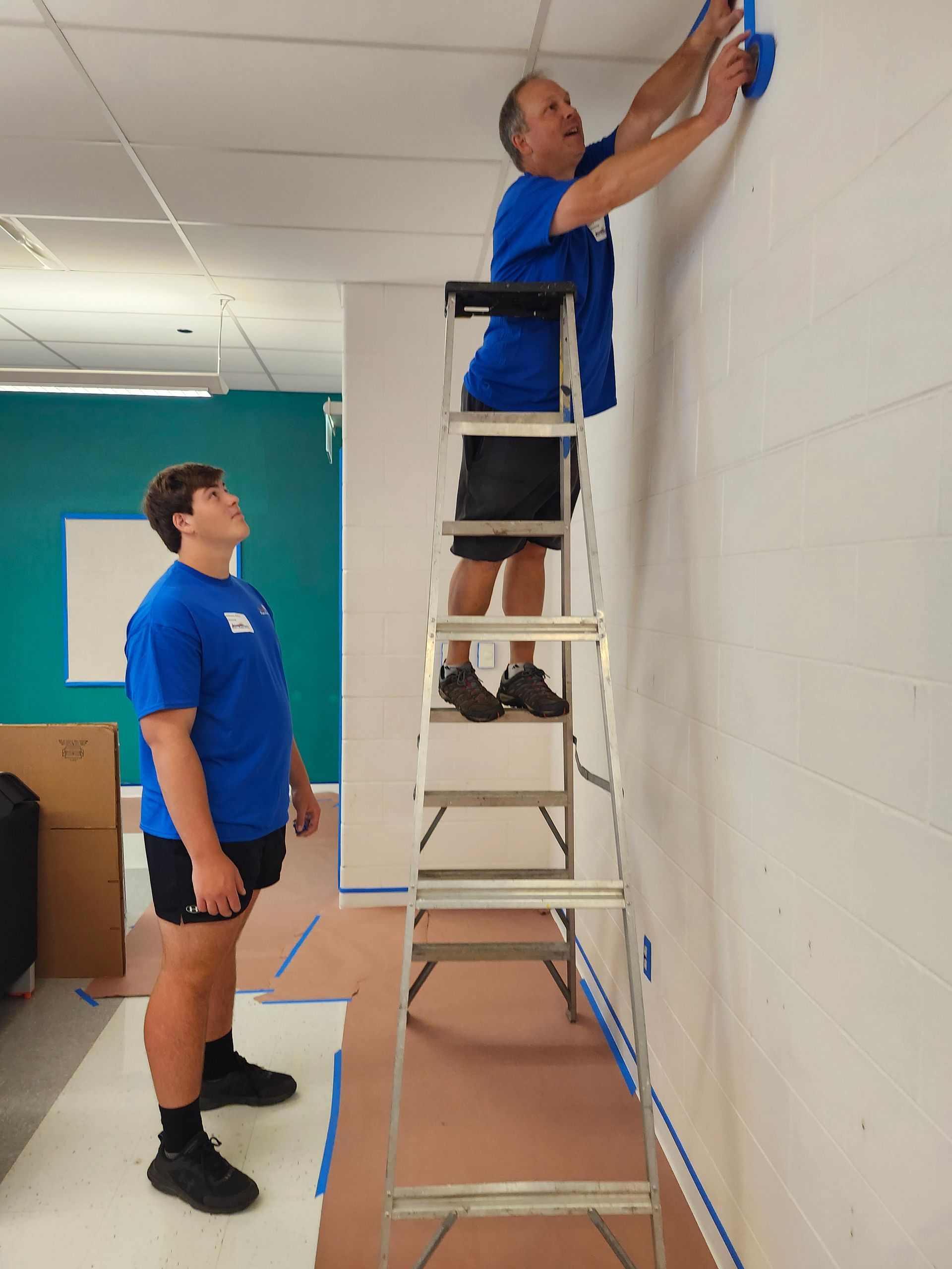 A man standing on a ladder painting a wall