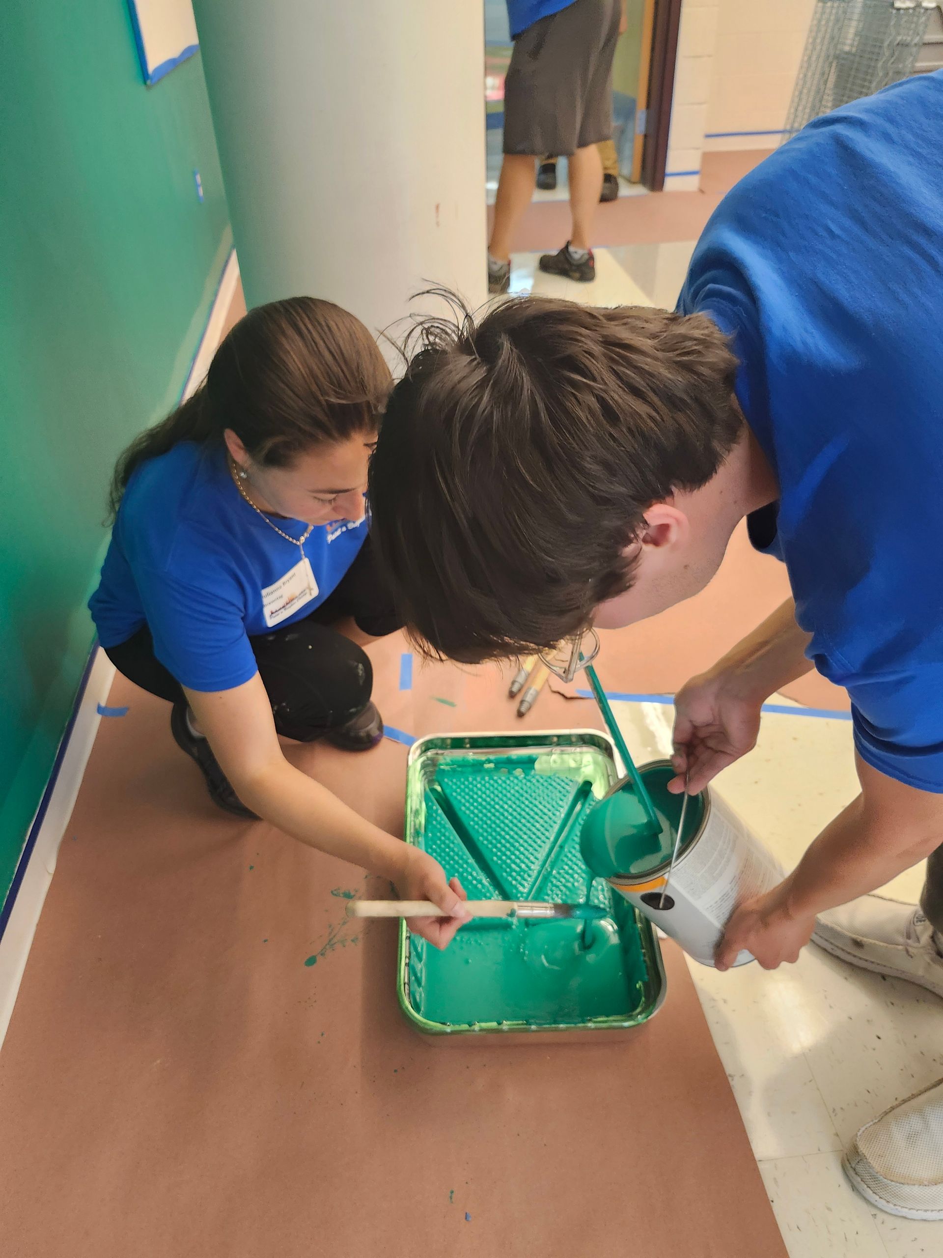 A man and a woman are painting a wall with green paint.