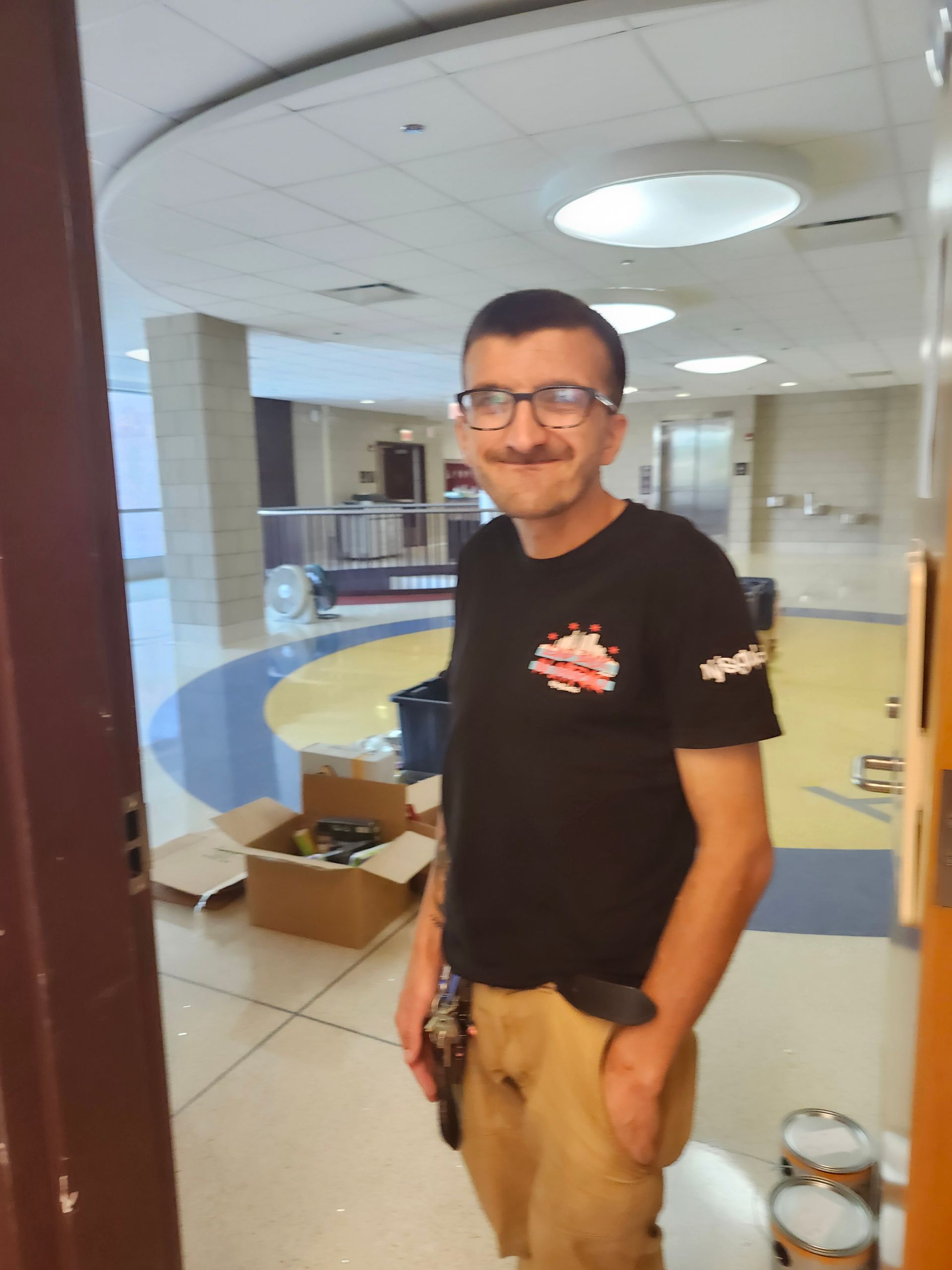A man wearing glasses and a black shirt is standing in a hallway