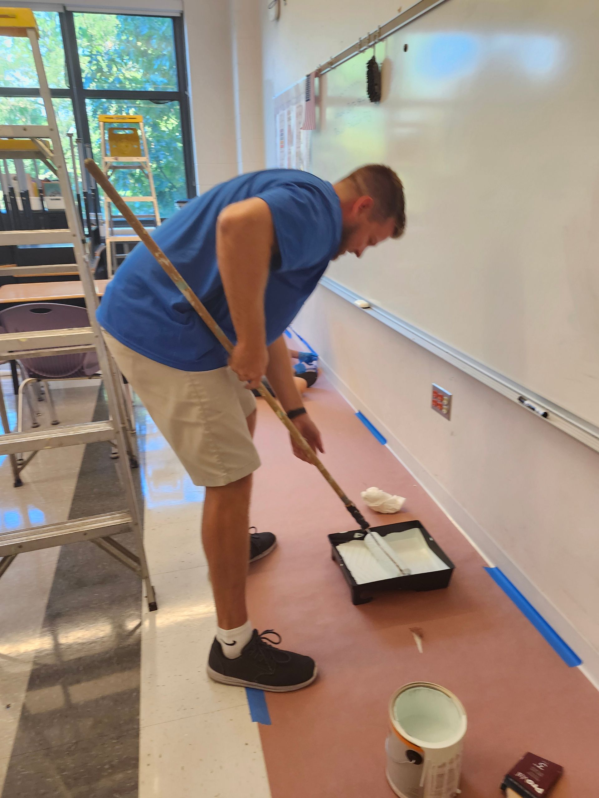 A man in a blue shirt is painting a wall in a classroom