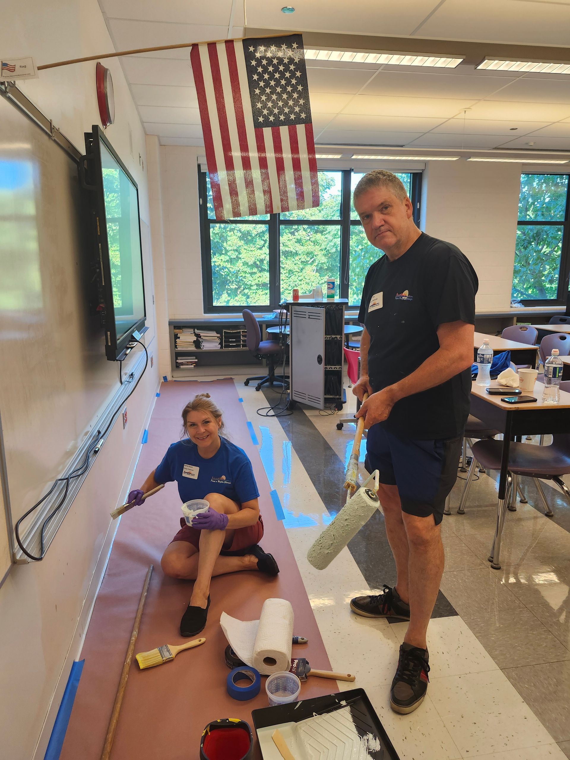 A man and a woman are painting a wall in a classroom.