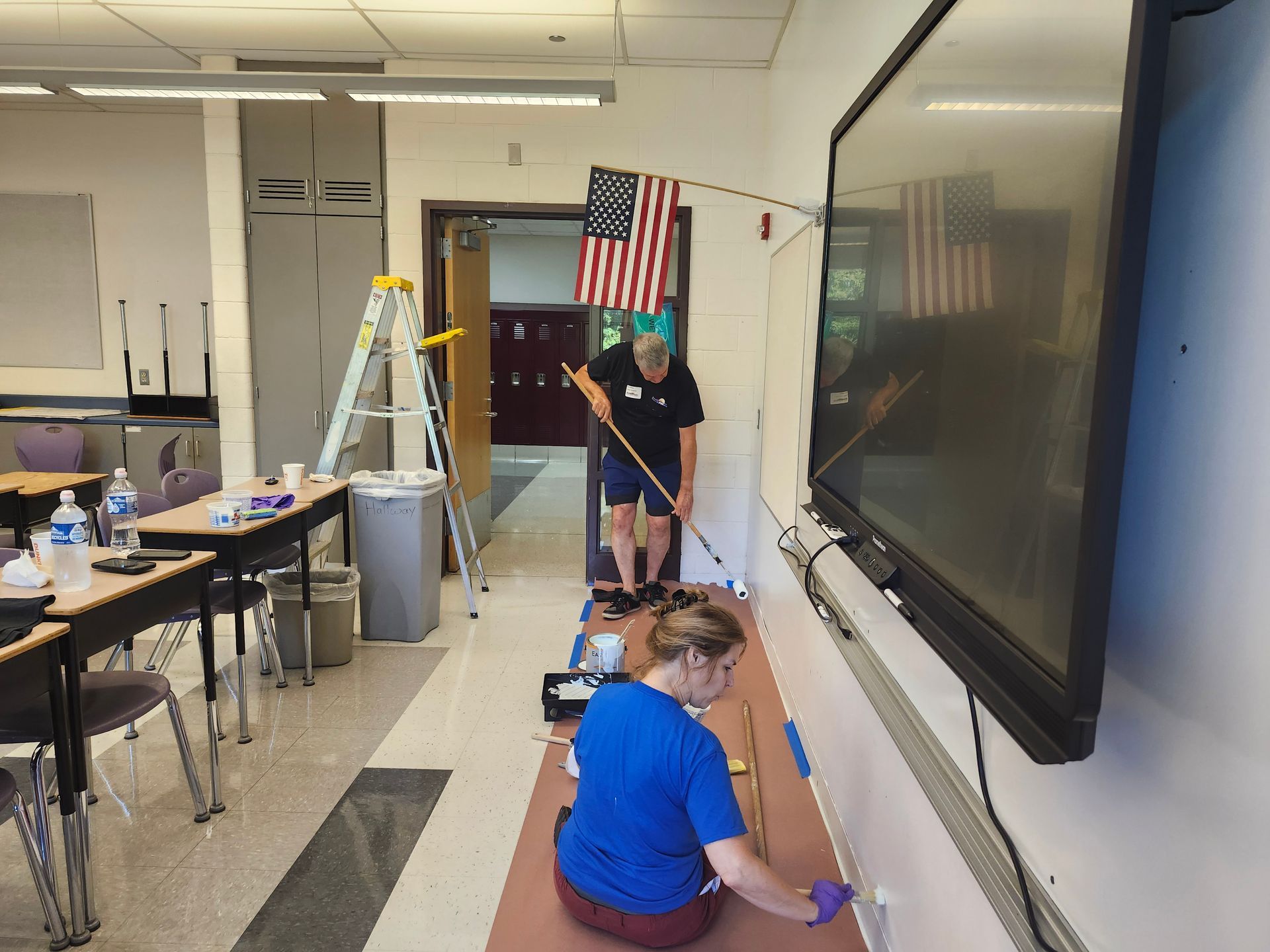 A woman in a blue shirt is painting a wall in a classroom