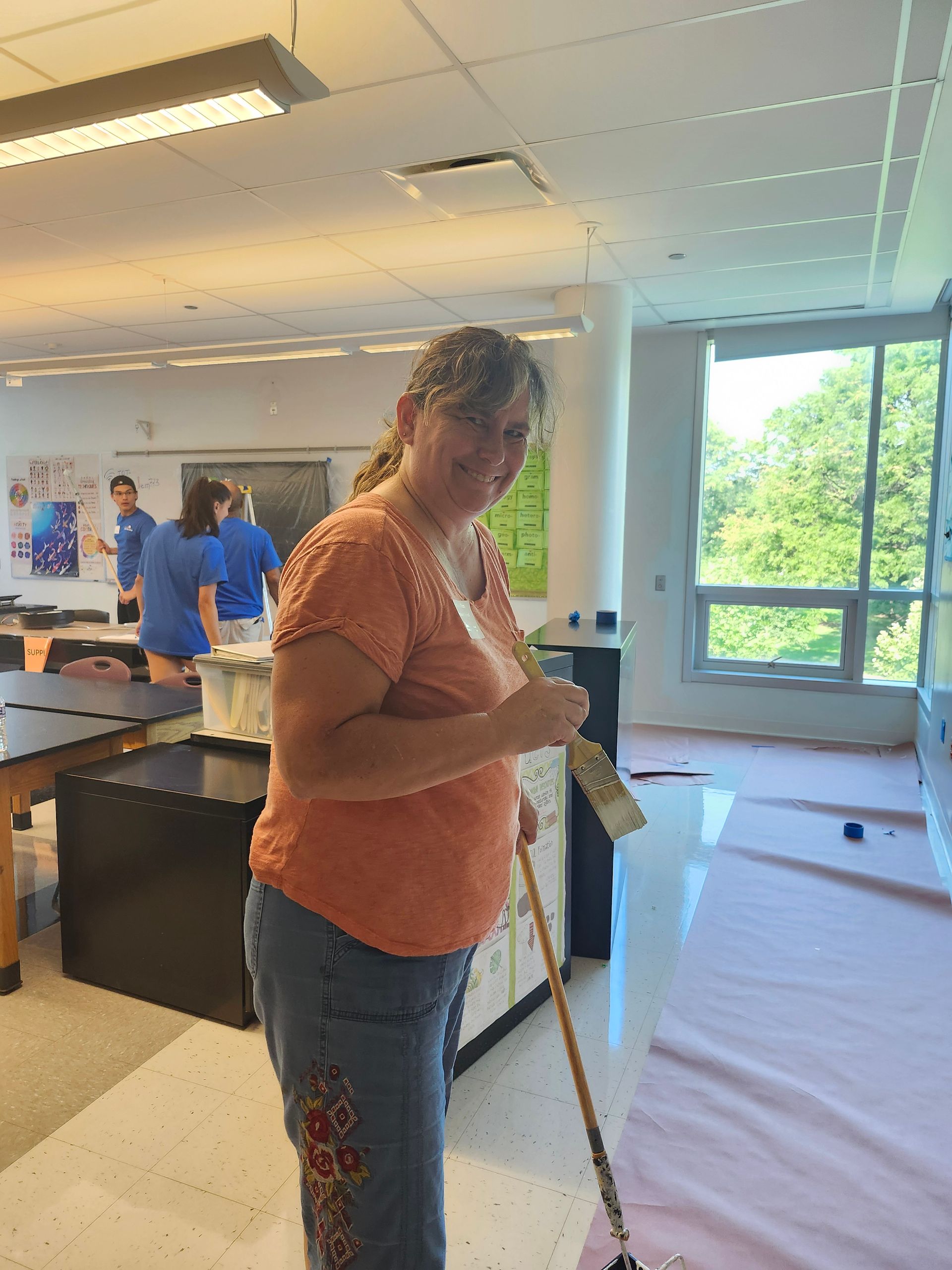 A woman is standing in a room holding a mop and a brush.