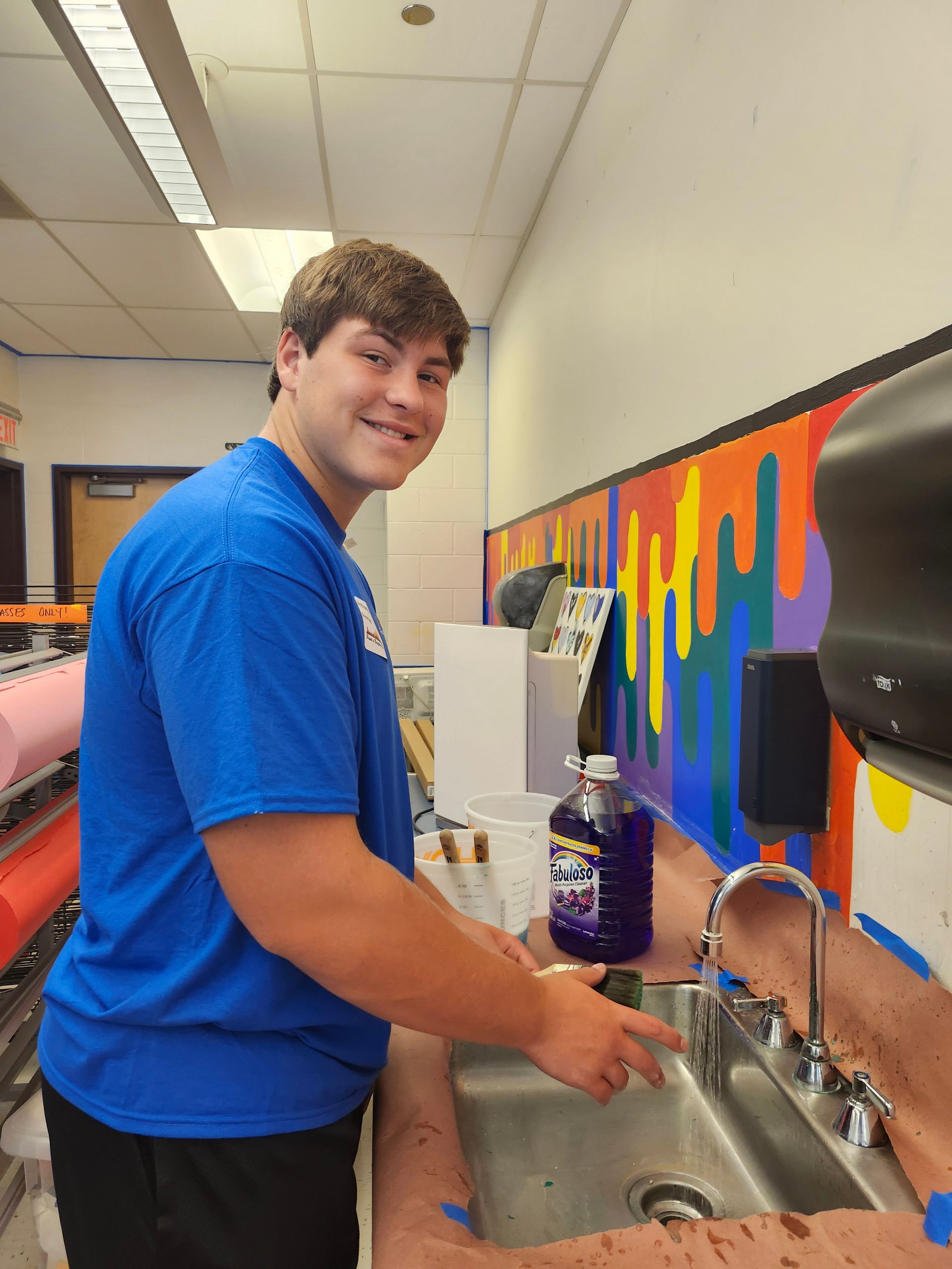 A man in a blue shirt is washing his hands in a sink.