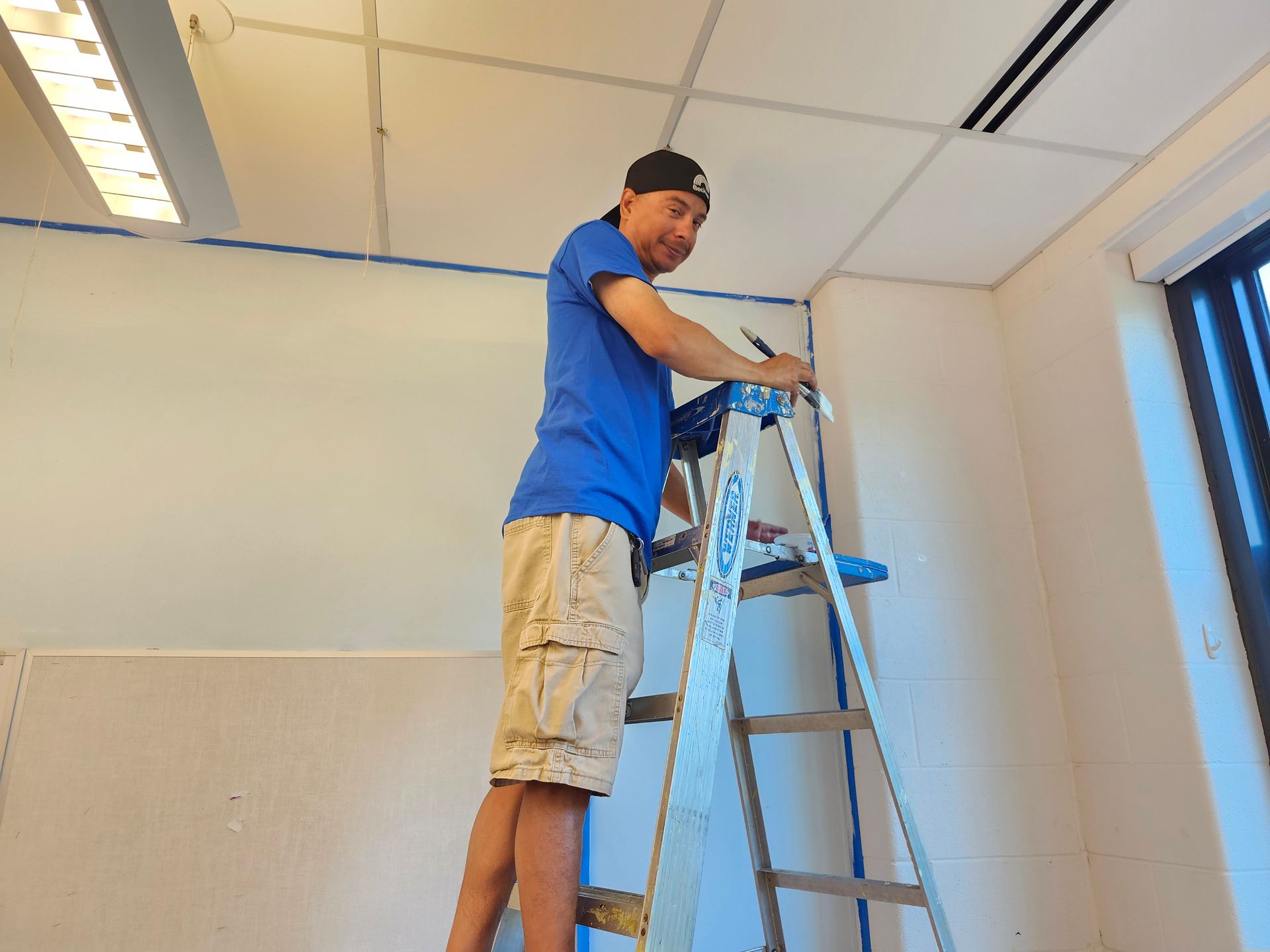 A man is standing on a ladder painting a wall