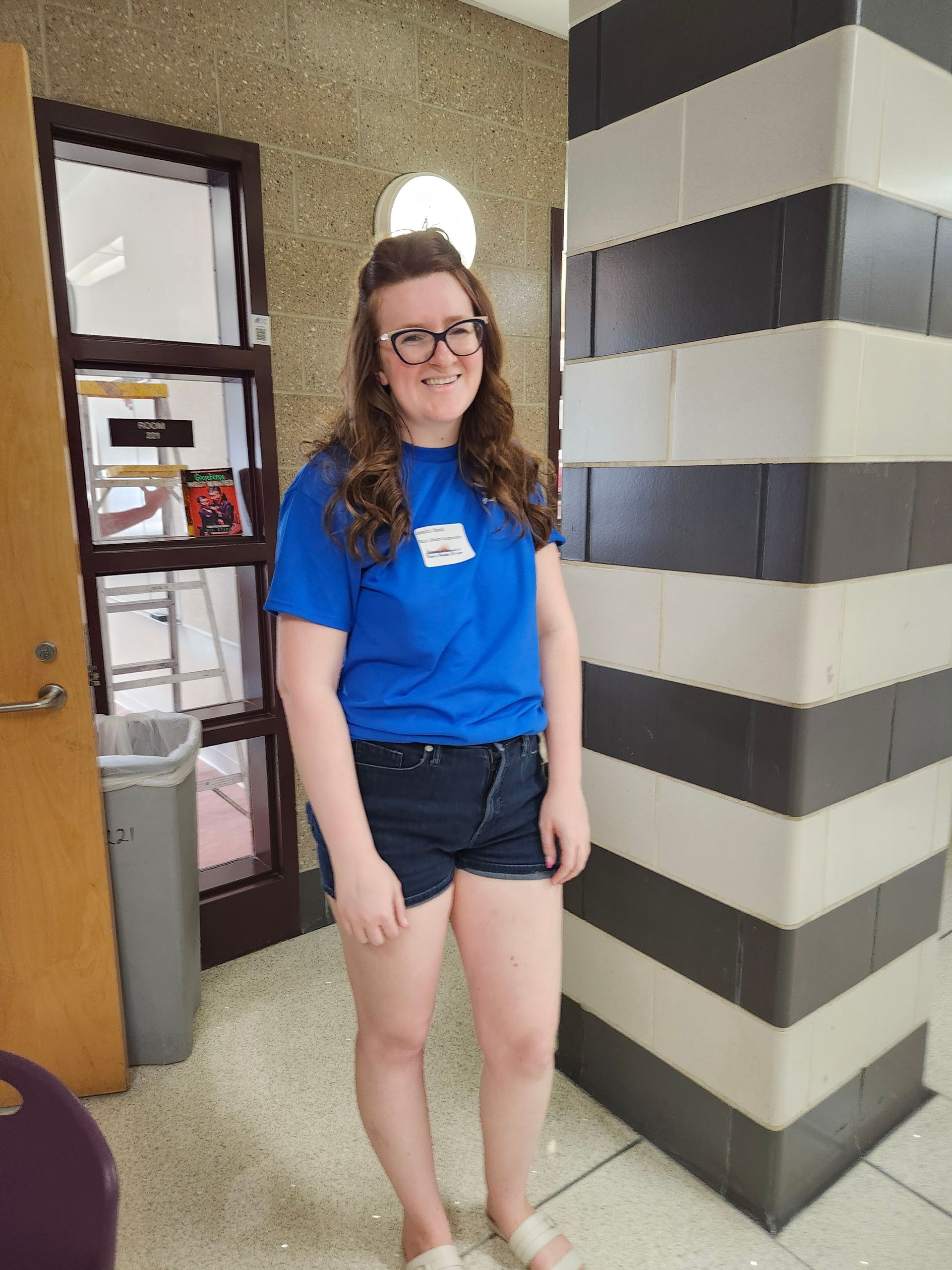 A girl in a blue shirt and shorts is standing in front of a striped wall.