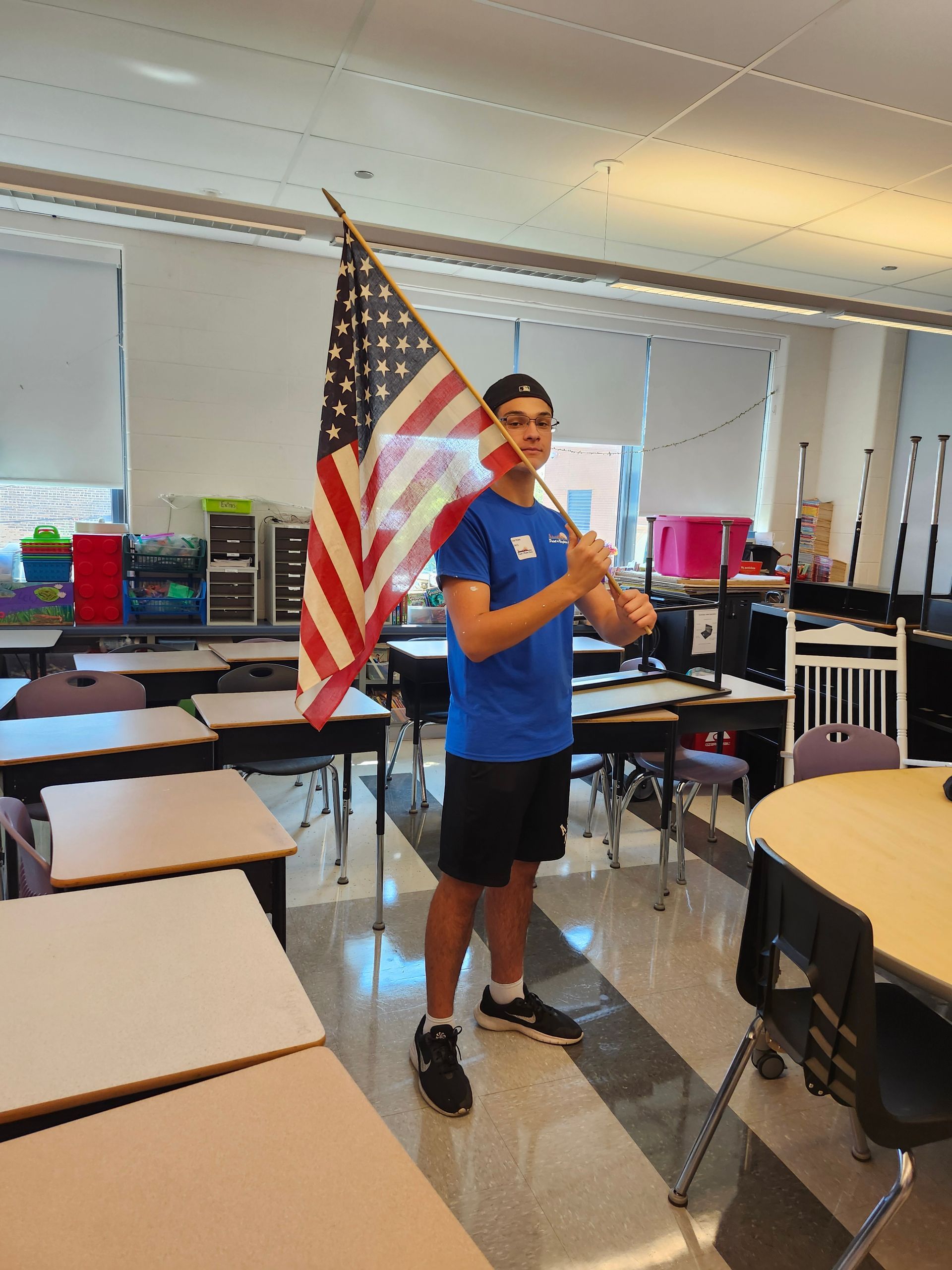A young man is holding an american flag in a classroom.