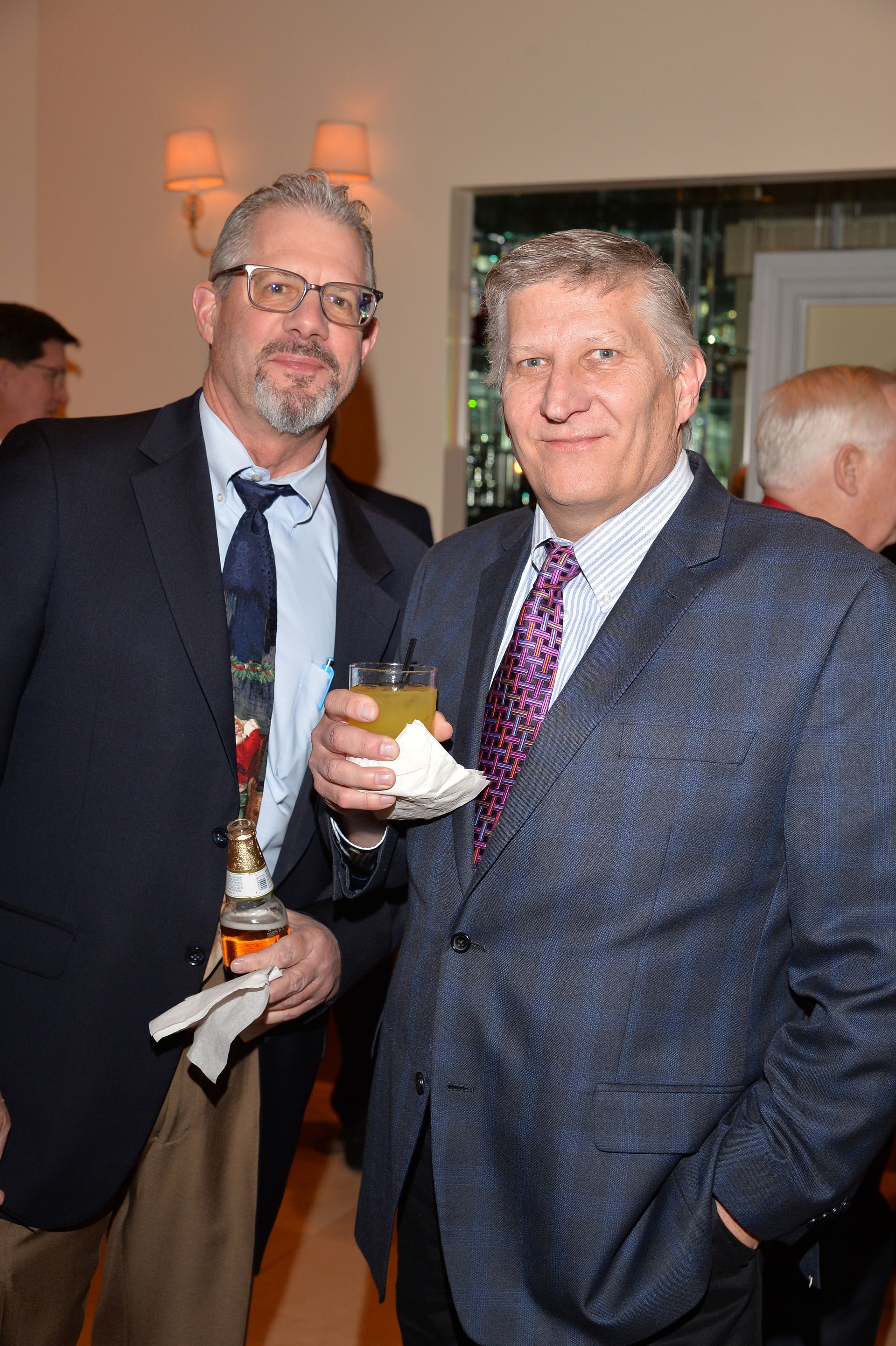 Two men in suits and ties are standing next to each other holding drinks.